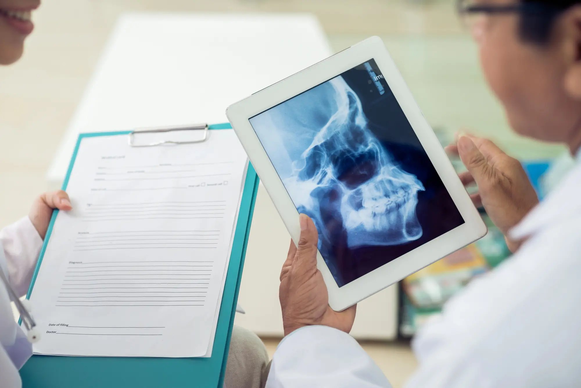 Doctor holding a tablet displaying a lateral skull X-ray while consulting with a patient holding a clipboard.