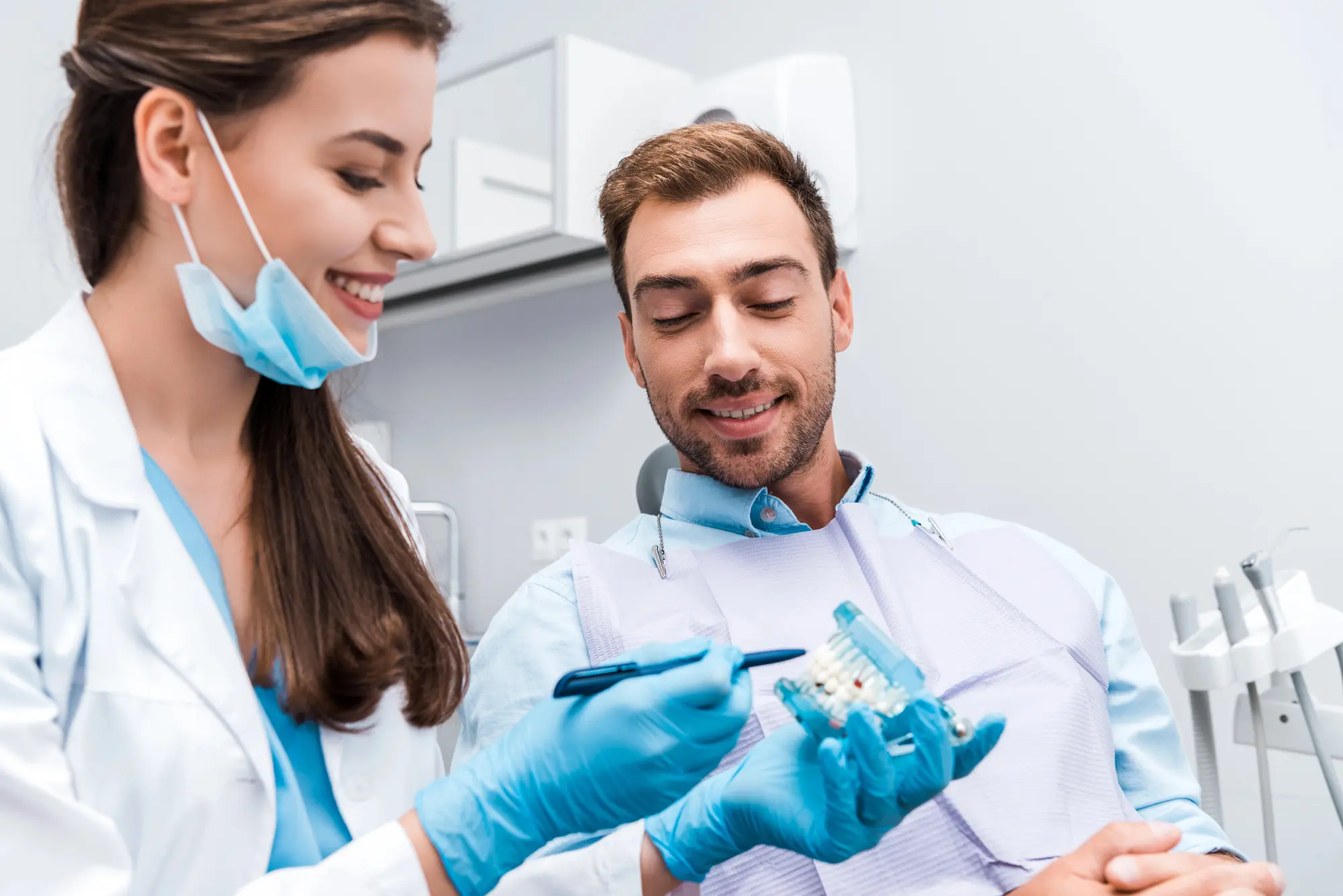 Smiling female dentist in gloves showing dental model to a male patient in a dental clinic.