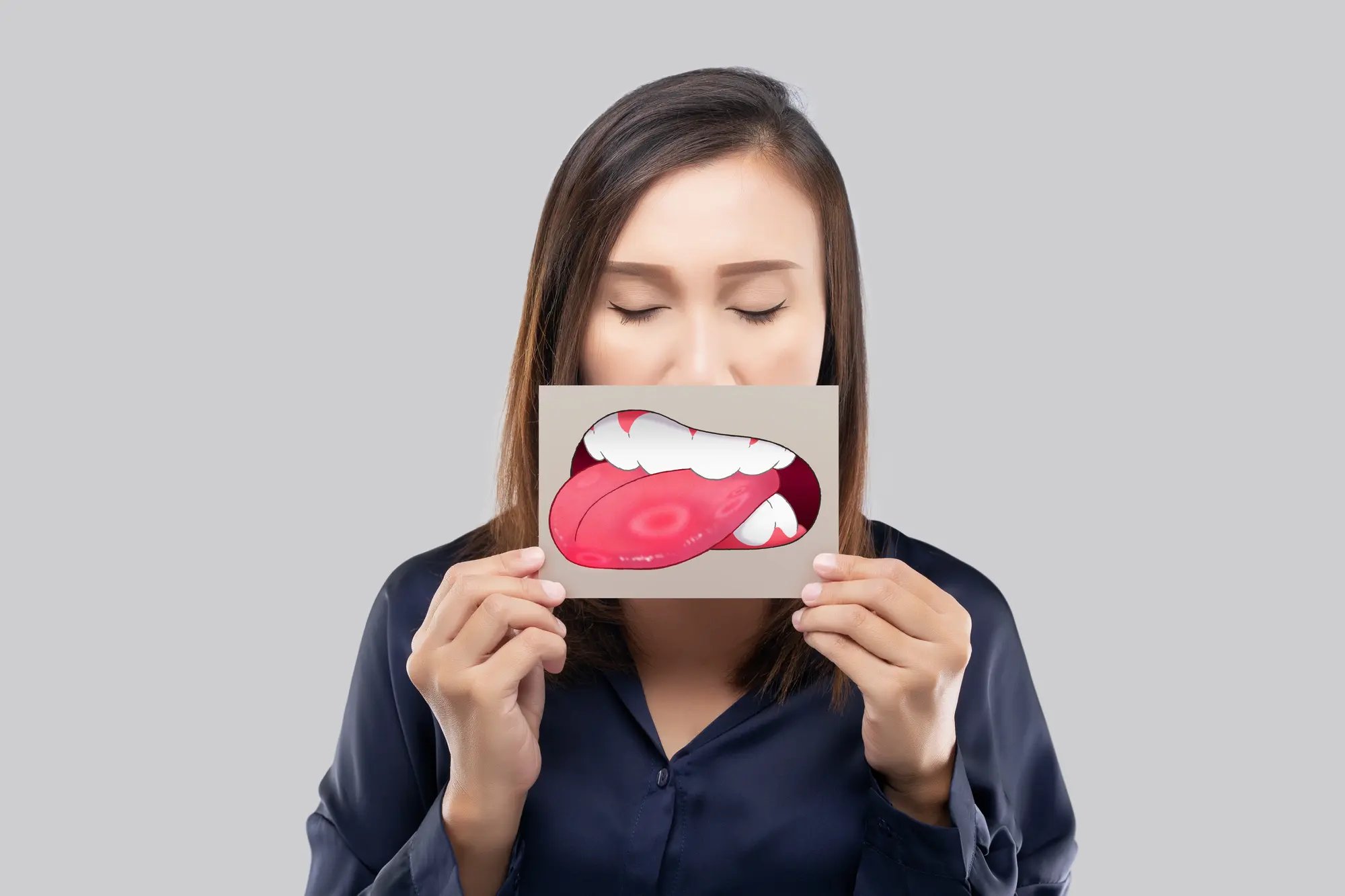 Woman with eyes closed holding a card in front of her mouth featuring a cartoon mouth with an open mouth and tongue sticking out.