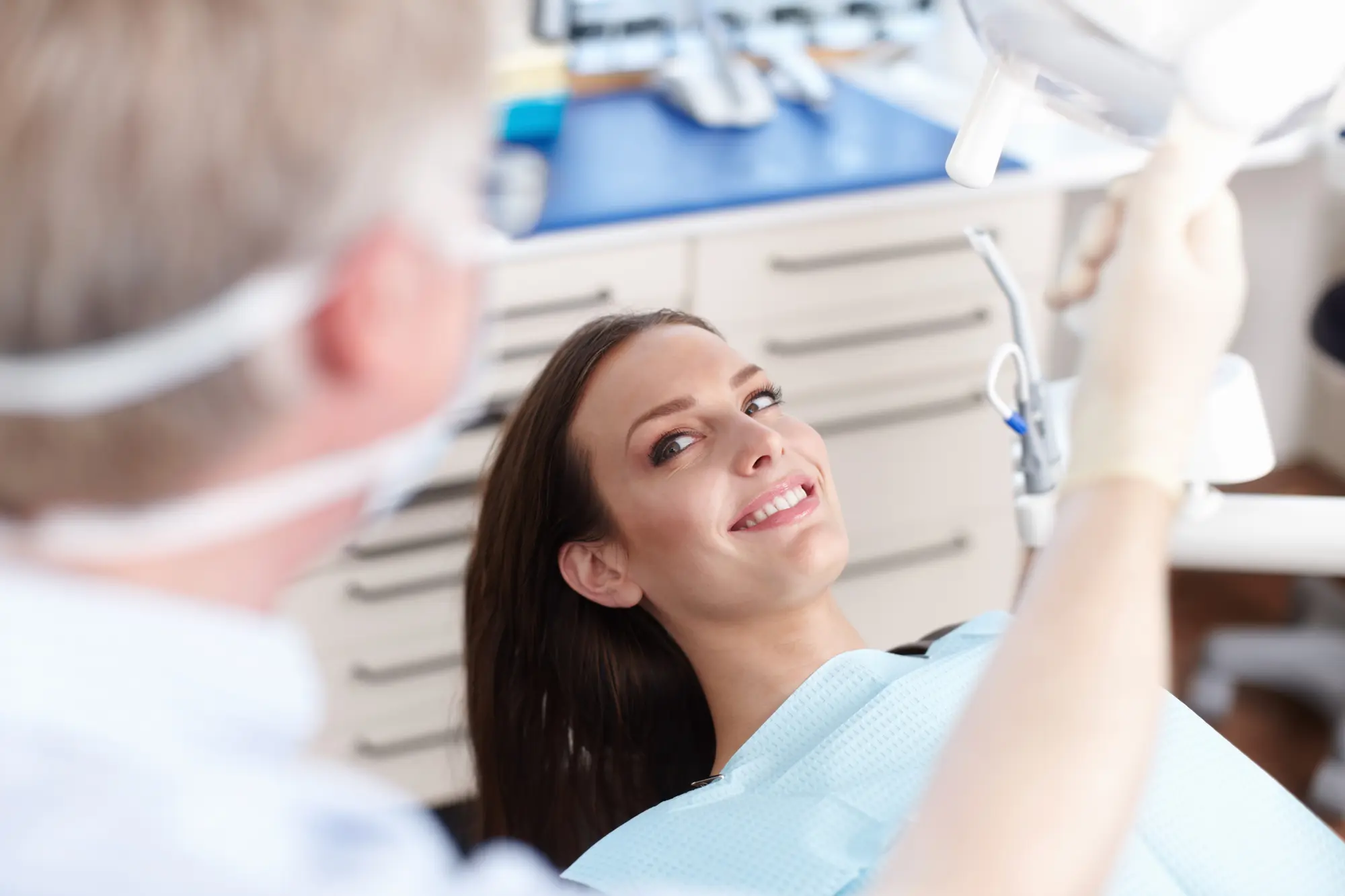 Smiling woman in a dental chair looking at a dentist adjusting a dental light in the clinic.