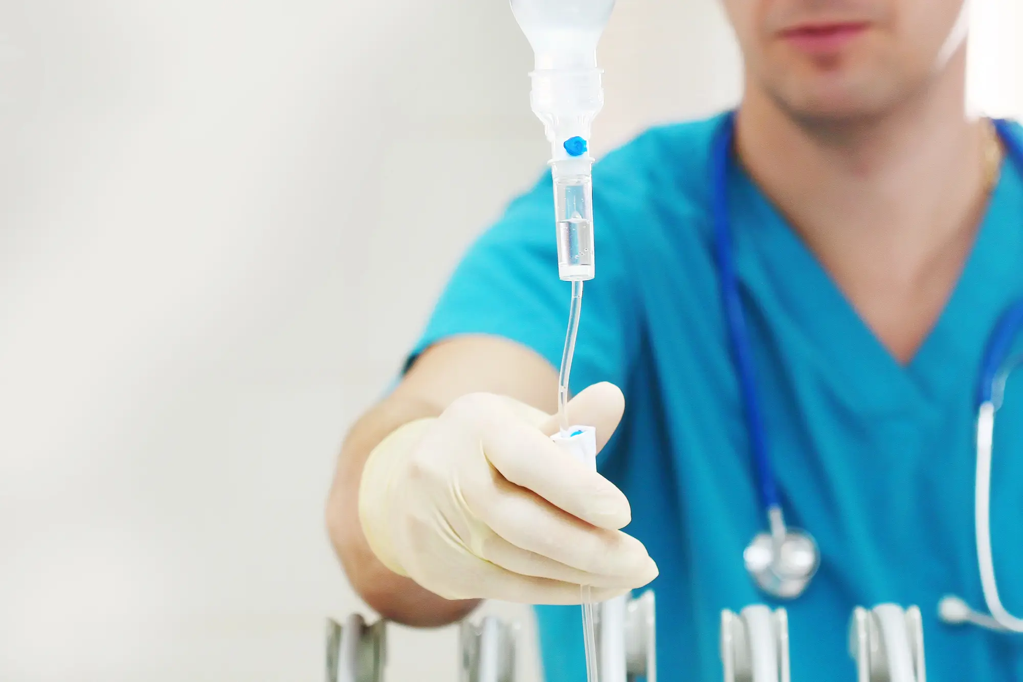 Healthcare professional in blue scrubs and gloves adjusting an IV drip.