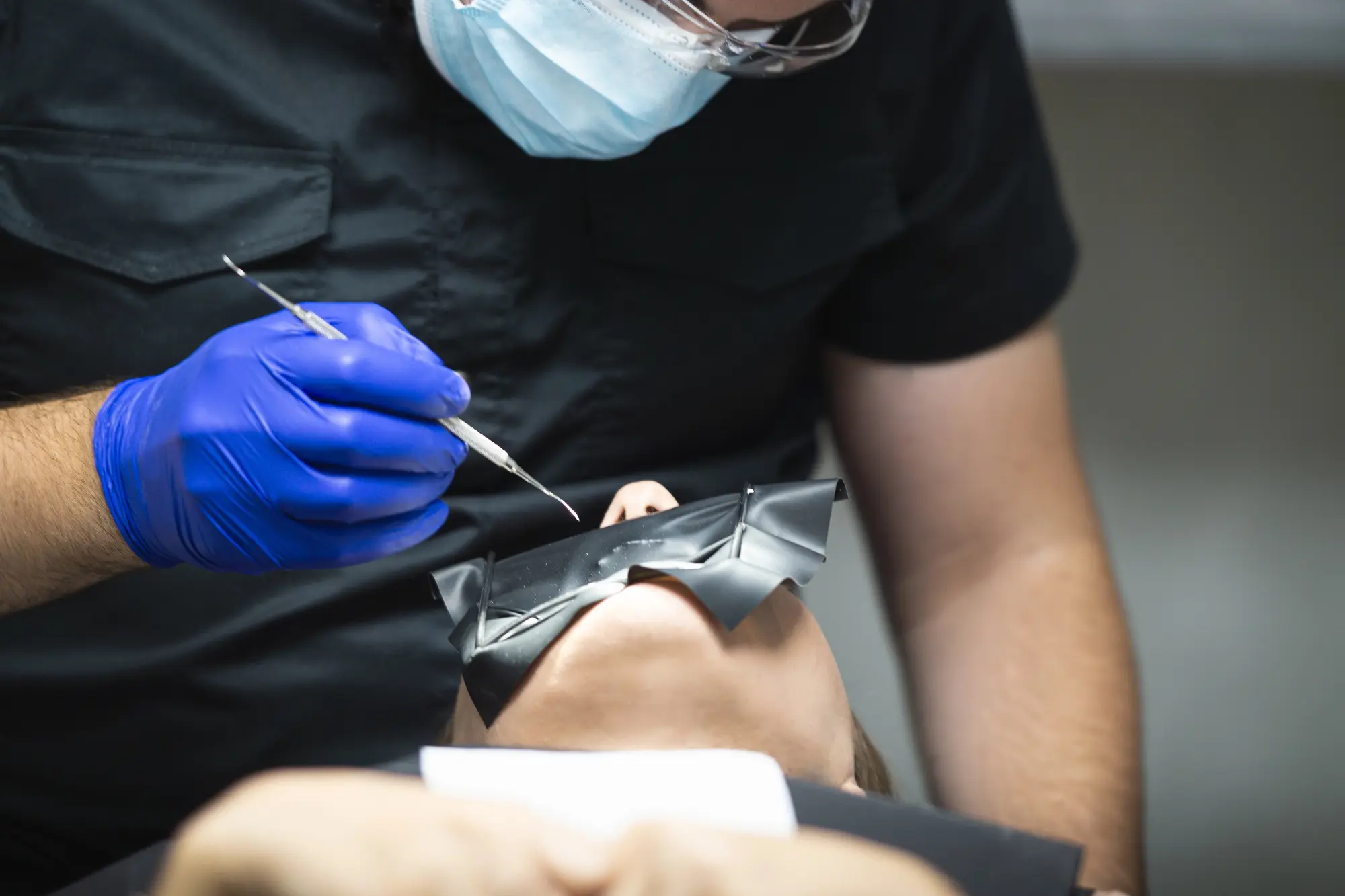 Dentist wearing blue gloves and protective glasses working on a patient with a dental dam in place.