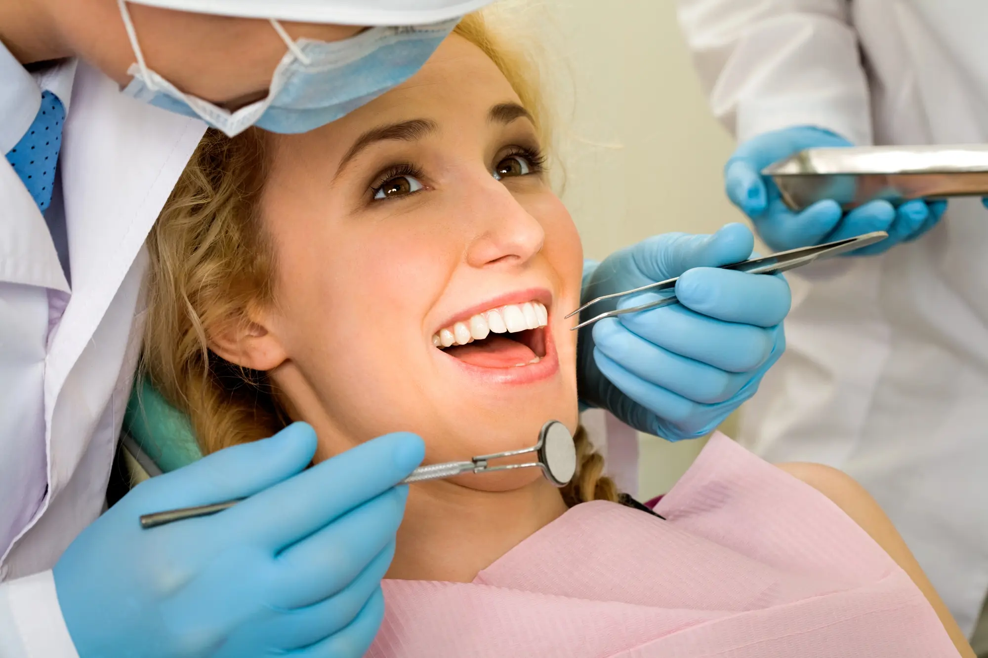 Smiling woman receiving dental examination from dentist wearing blue gloves and face mask.