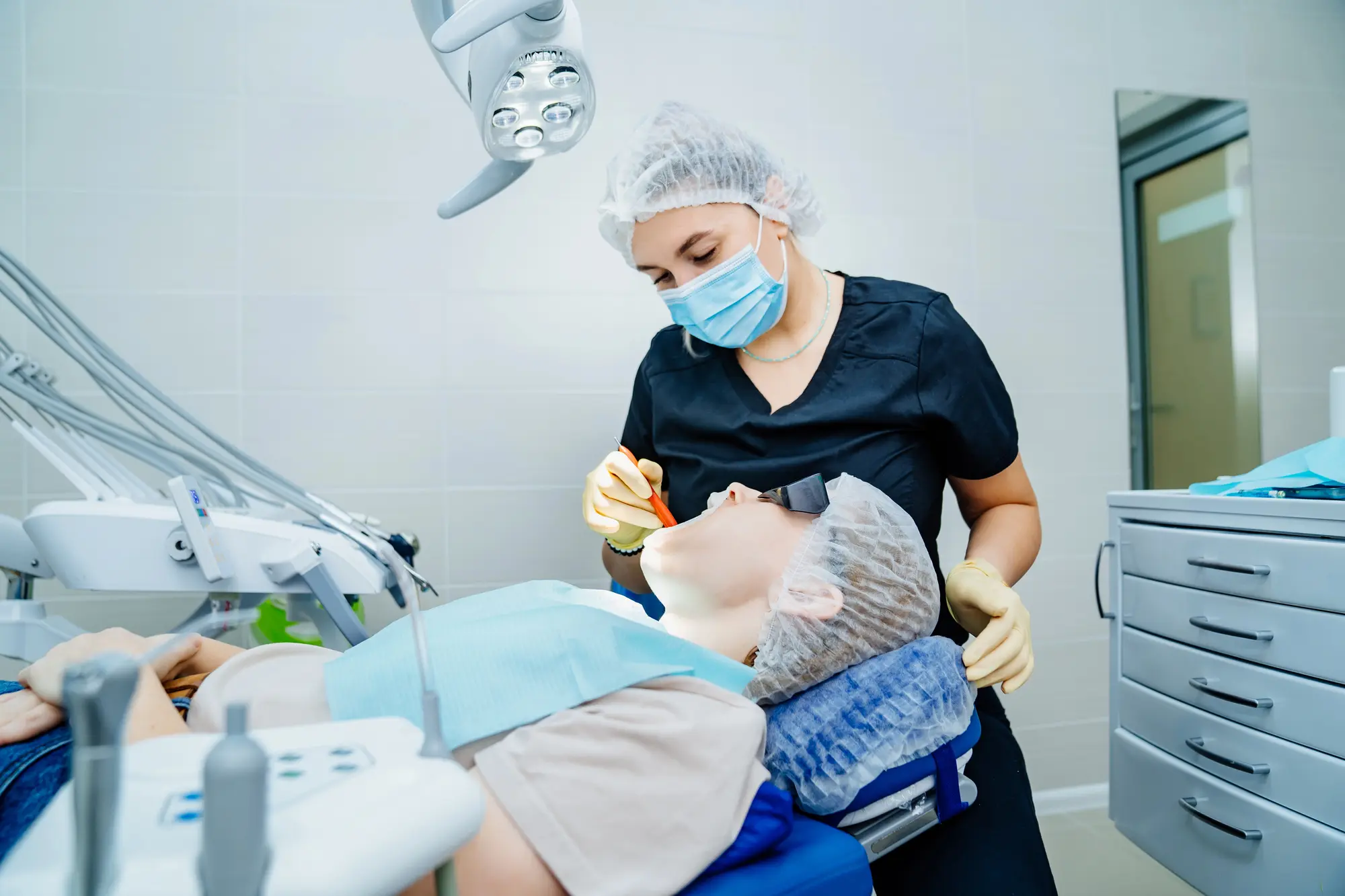 Dentist in a blue uniform and mask examining a patient's mouth in a dental clinic.