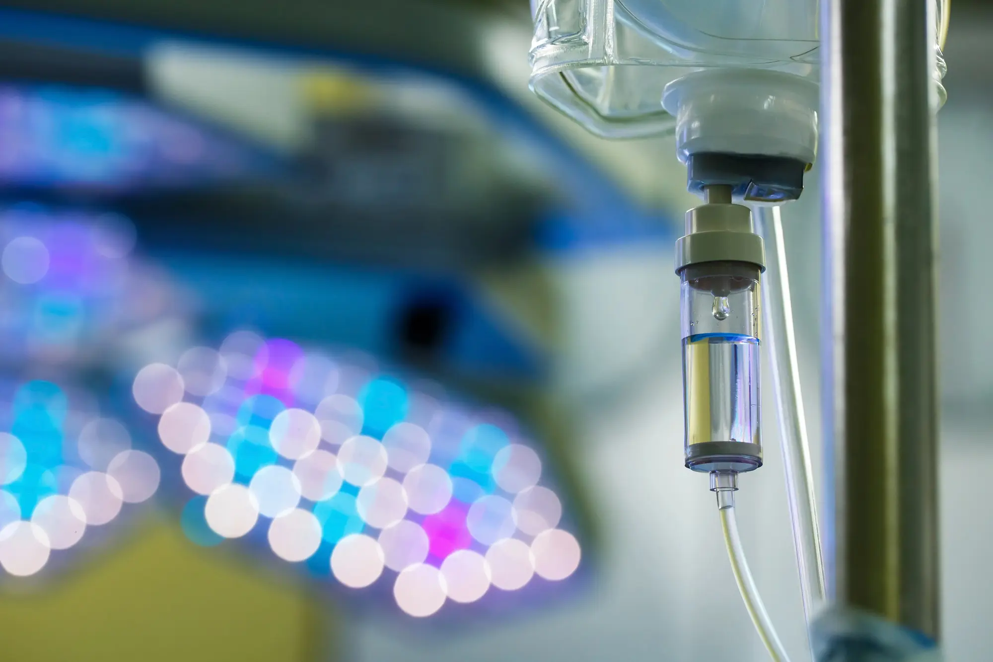 Close-up of an intravenous drip chamber with a drop of fluid in a medical setting.