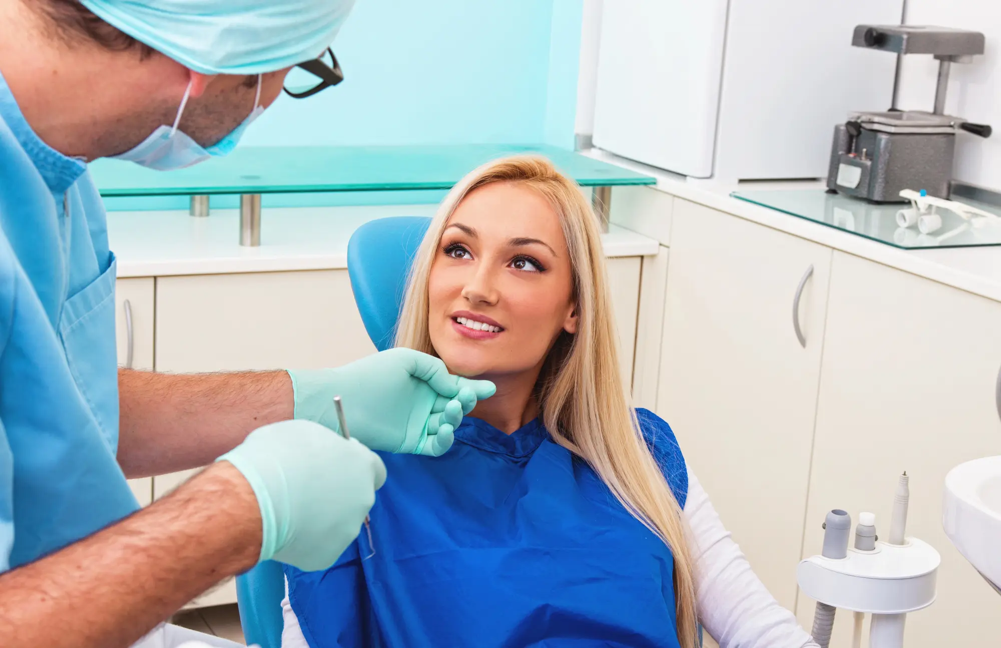 Dentist wearing gloves and a mask consulting a smiling female patient in a dental chair.
