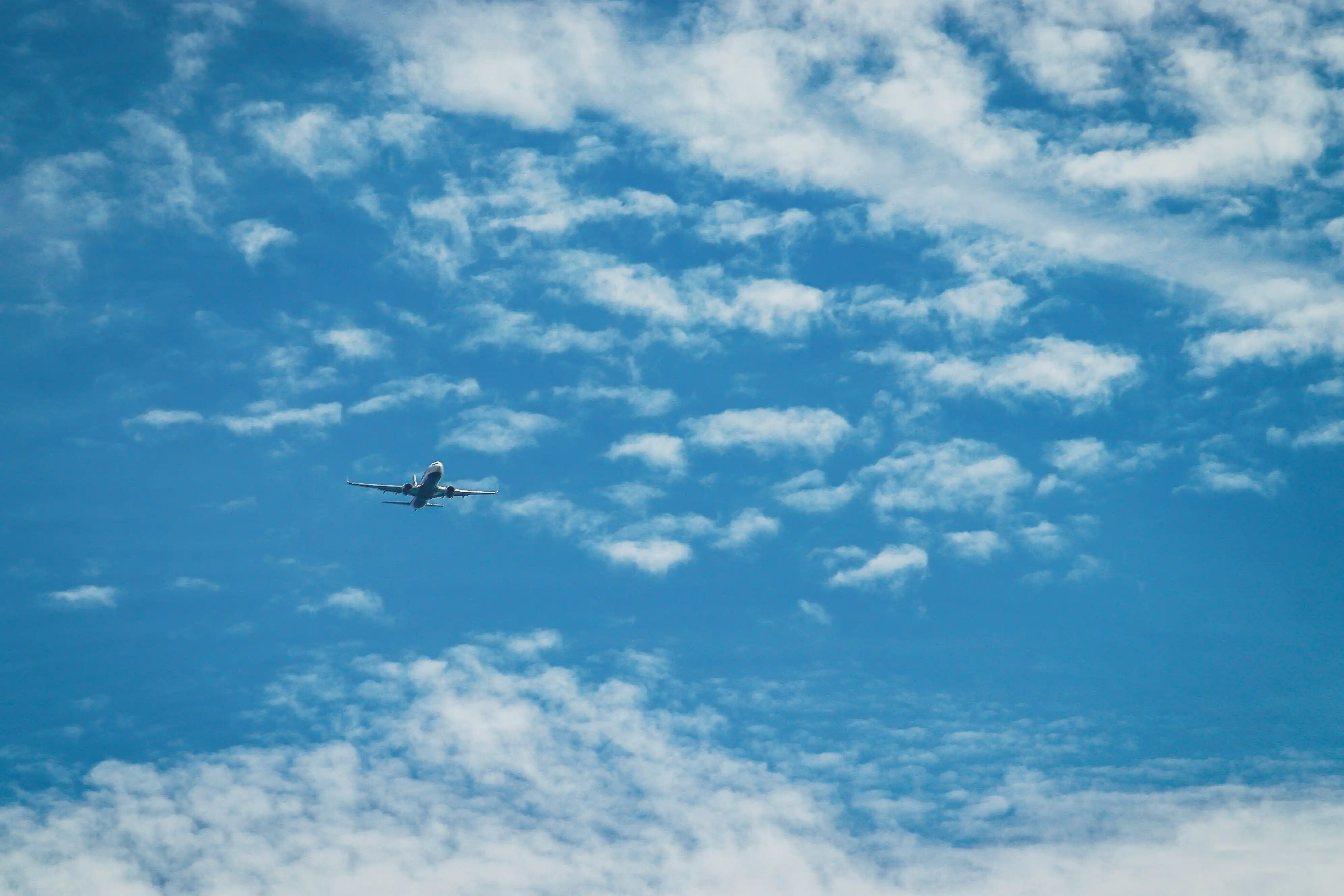 Airplane flying in a blue sky with scattered white clouds.
