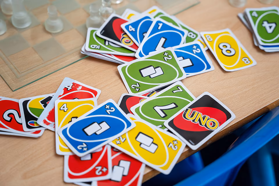 A pile of colourful UNO cards scattered on a wooden table with part of a chessboard visible.