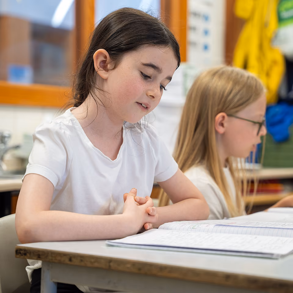 A girl and a boy sitting at a table reading and studying notebooks in a classroom setting.
