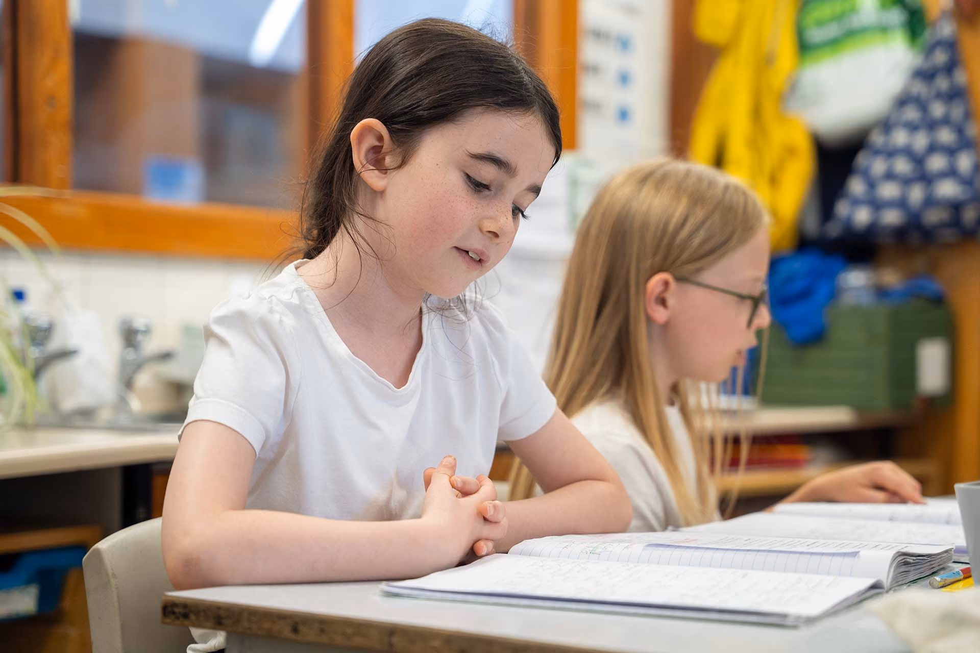 A girl and a boy sitting at a table reading and studying notebooks in a classroom setting.