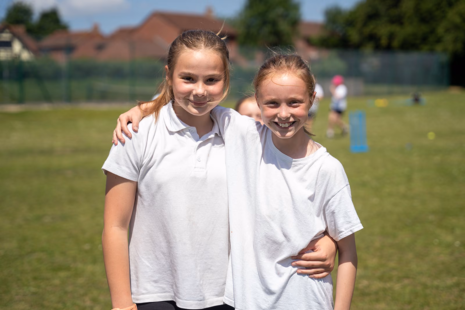 Two smiling pupils standing arm in arm on the playing field during a sports session.