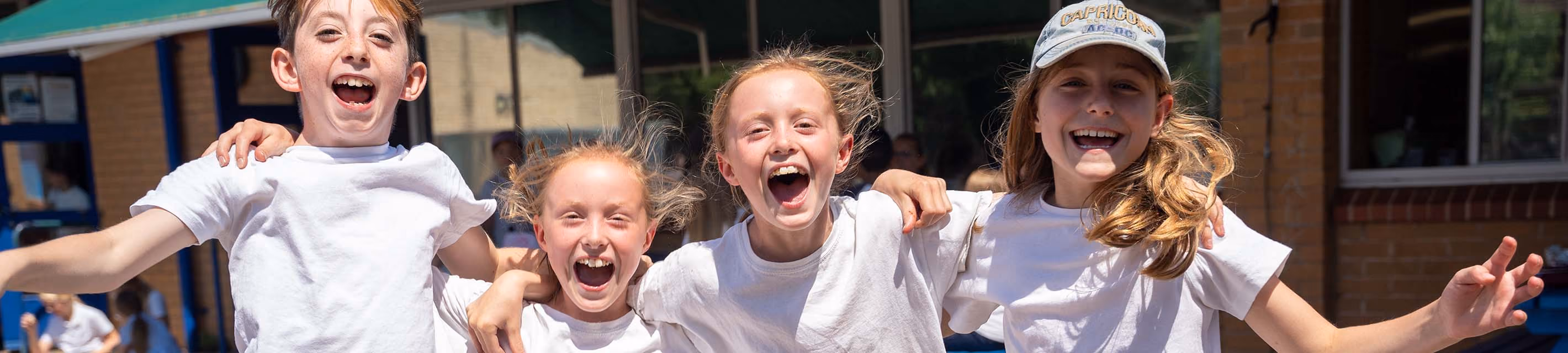 Four pupils laughing with arms around each other outside the school on a sunny day.