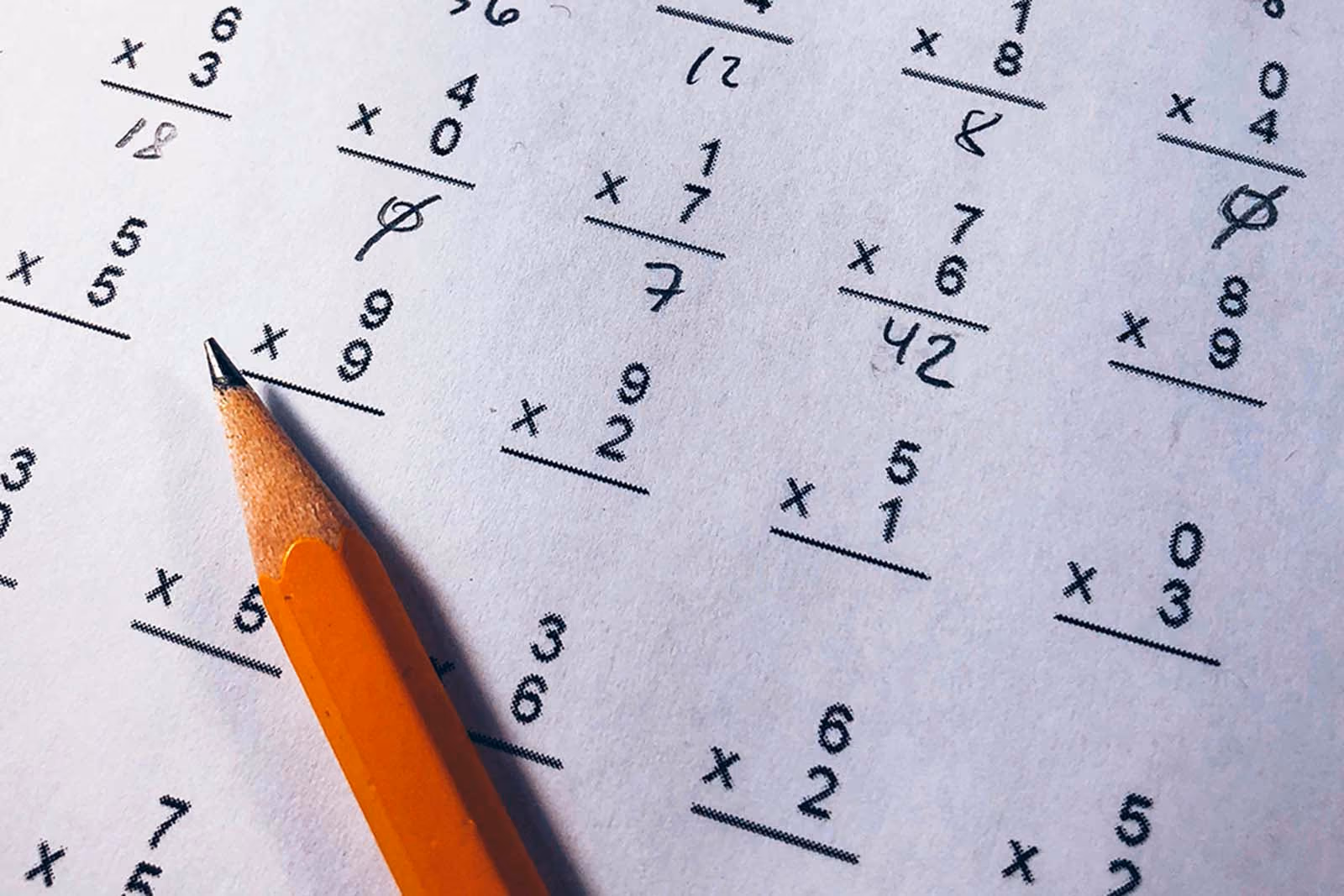 Close-up of a pencil resting on a worksheet of handwritten multiplication sums.