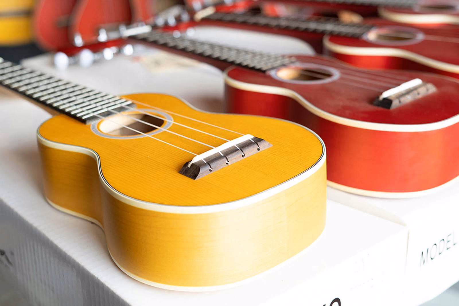 Row of ukuleles in yellow and red finishes lined up on a table.