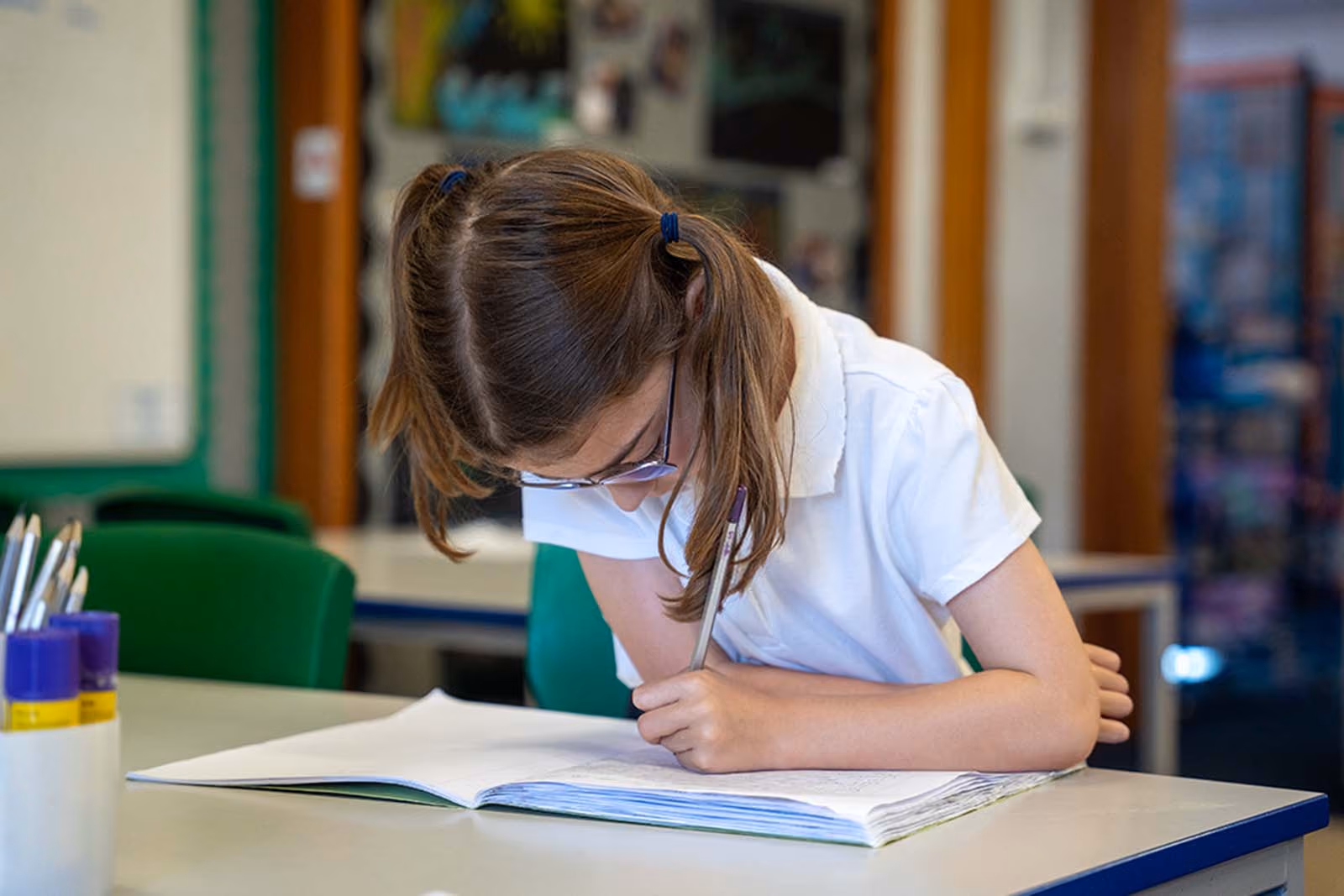 Pupil in glasses writing carefully in an exercise book at her desk.