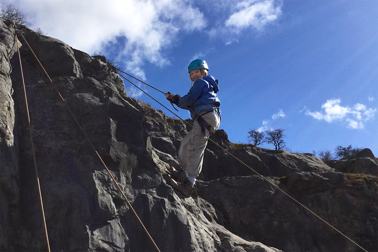 Pupil wearing a helmet and harness abseiling down a rock face on a residential trip.
