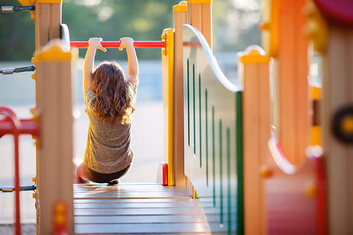 Child hanging from monkey bars on outdoor playground equipment.