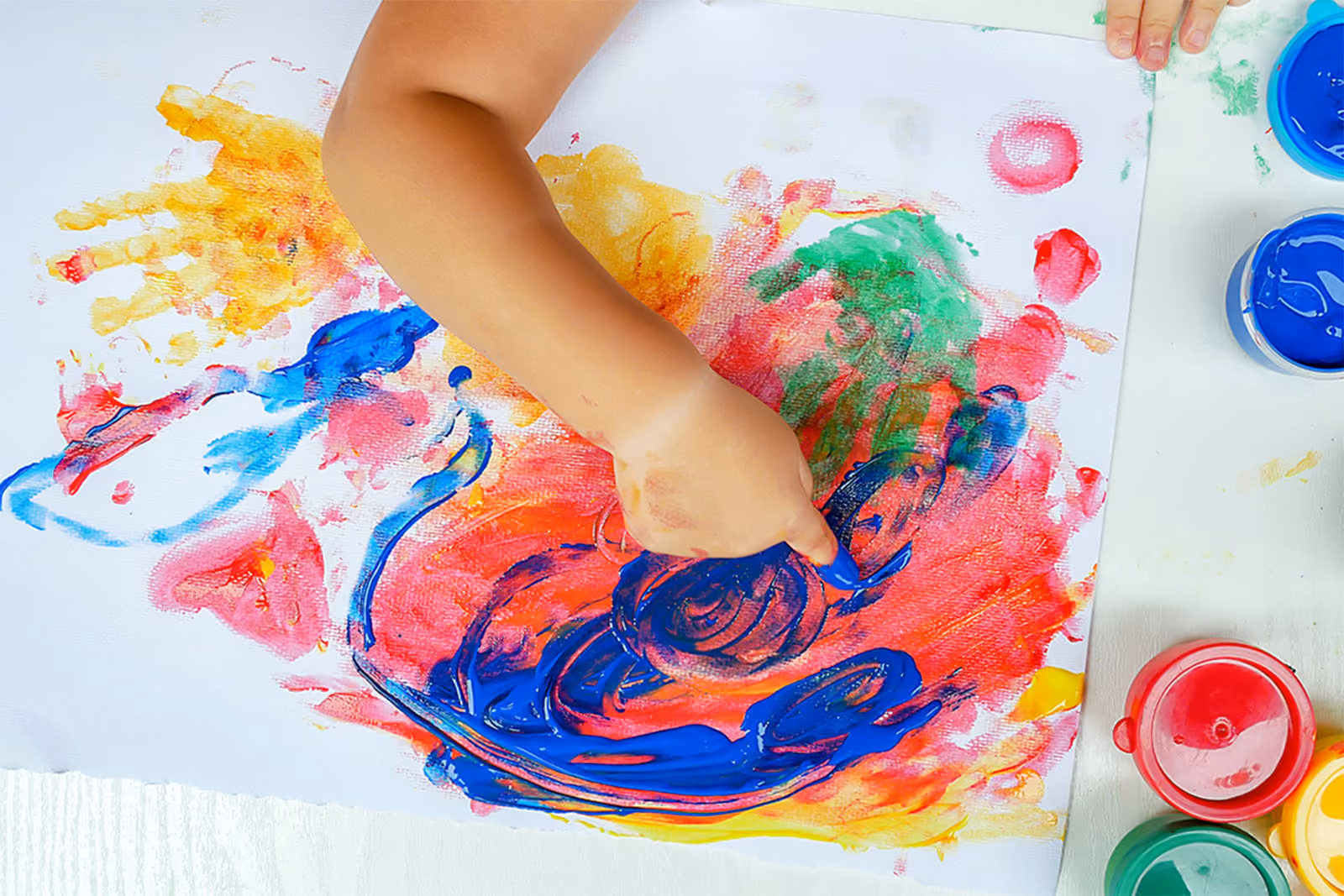 Young child's arm covered in colourful finger paint on paper.