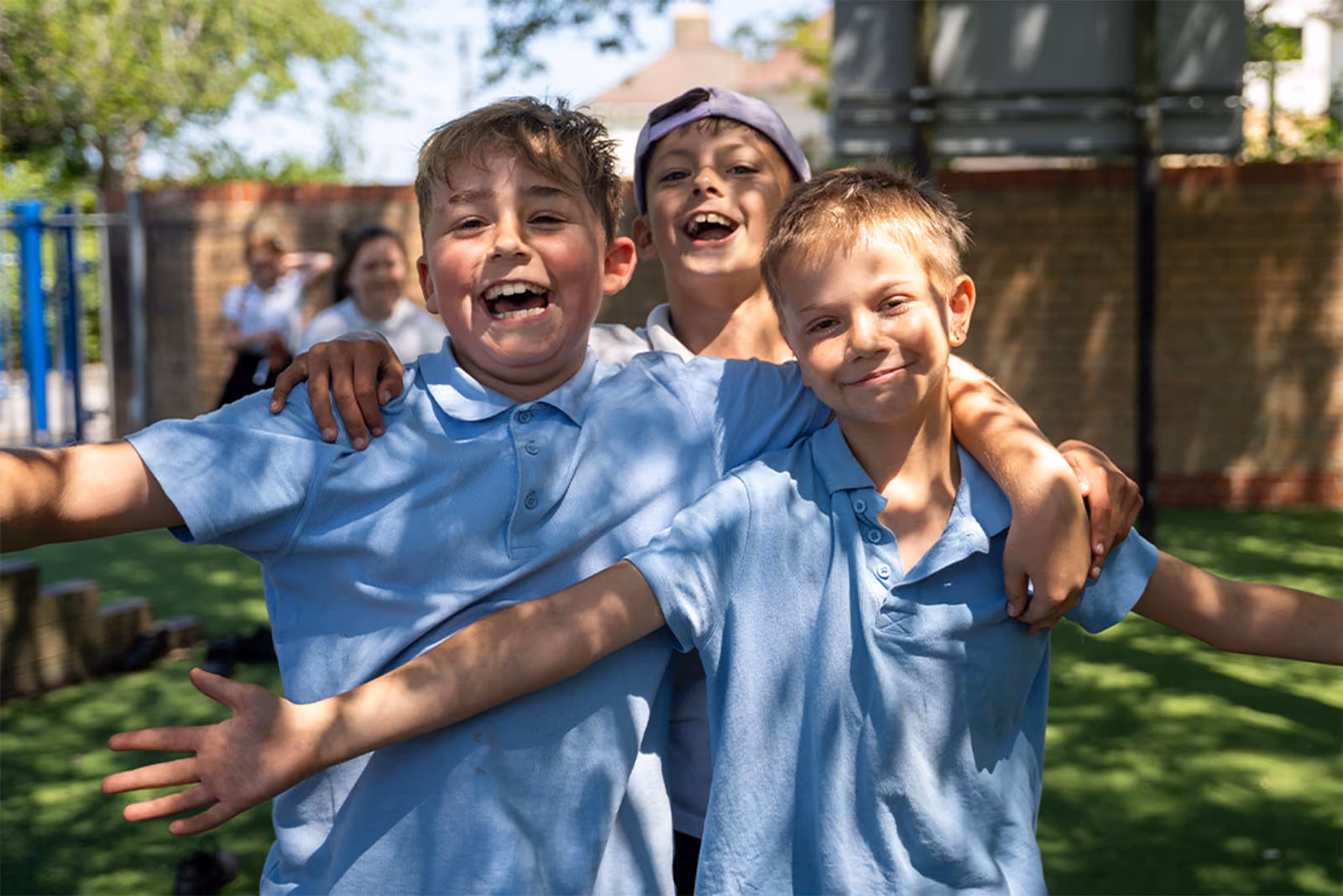 Three laughing pupils with arms around each other outdoors.