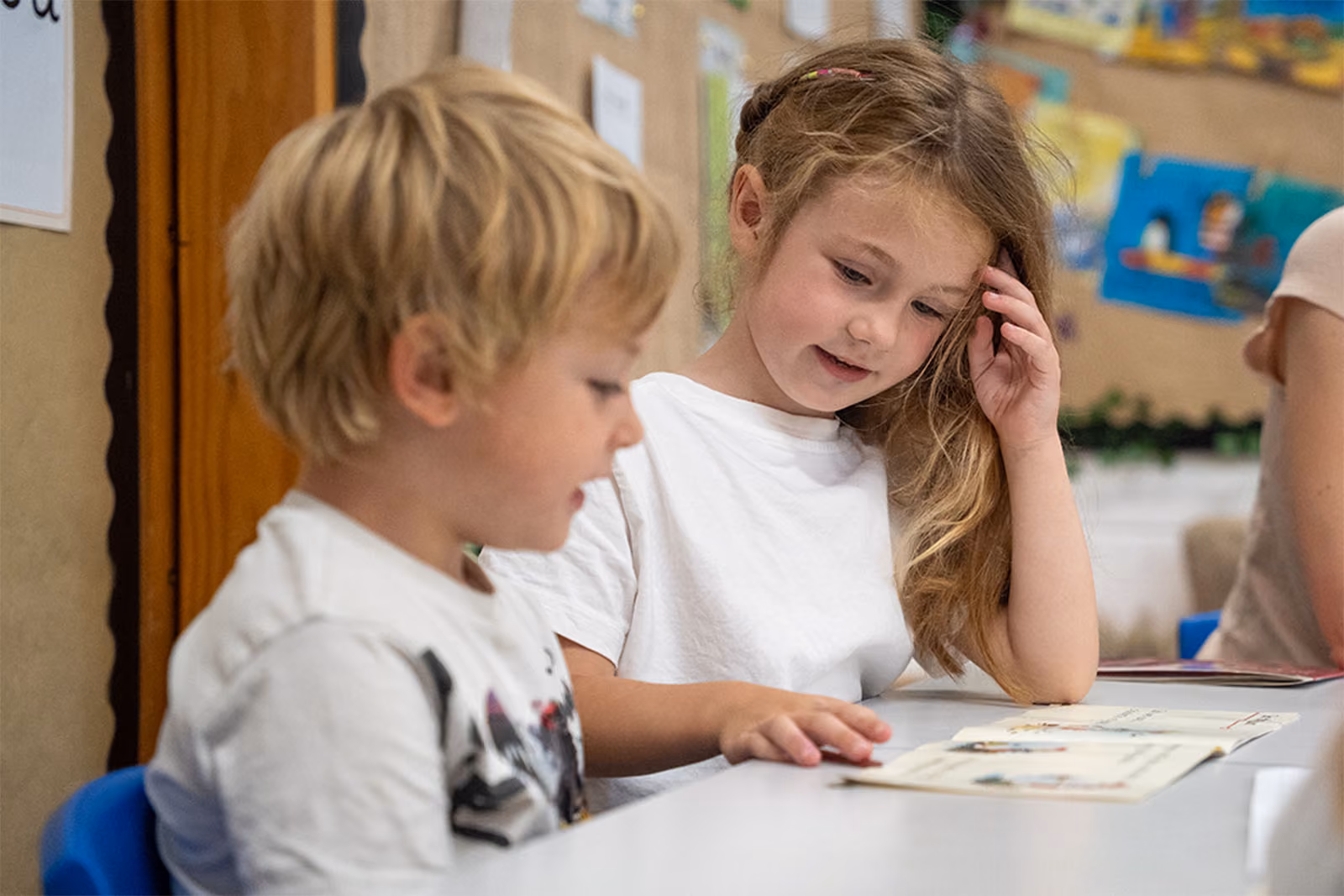 Two young pupils reading a book together at a table.