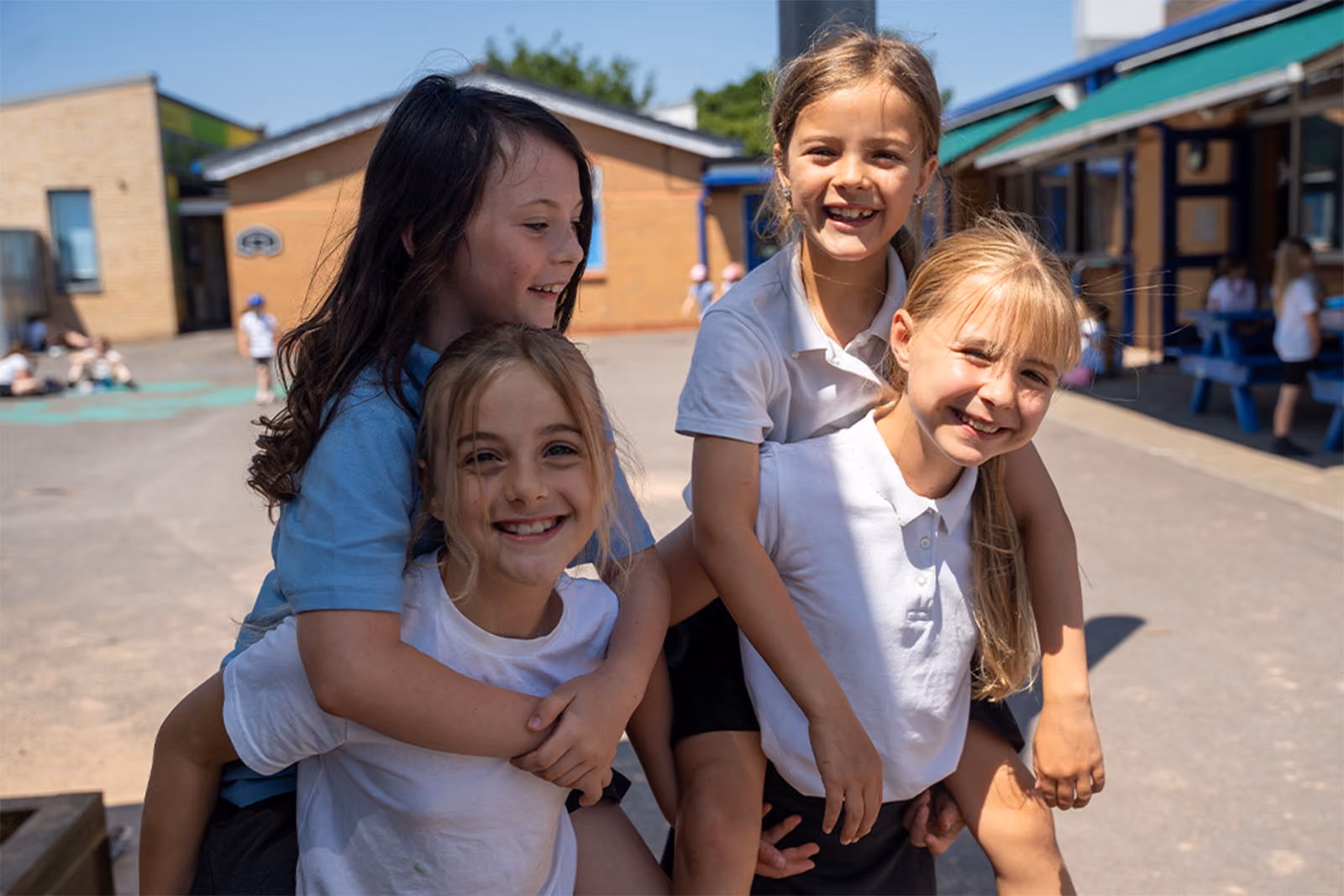 Four smiling pupils piggybacking each other in the playground.