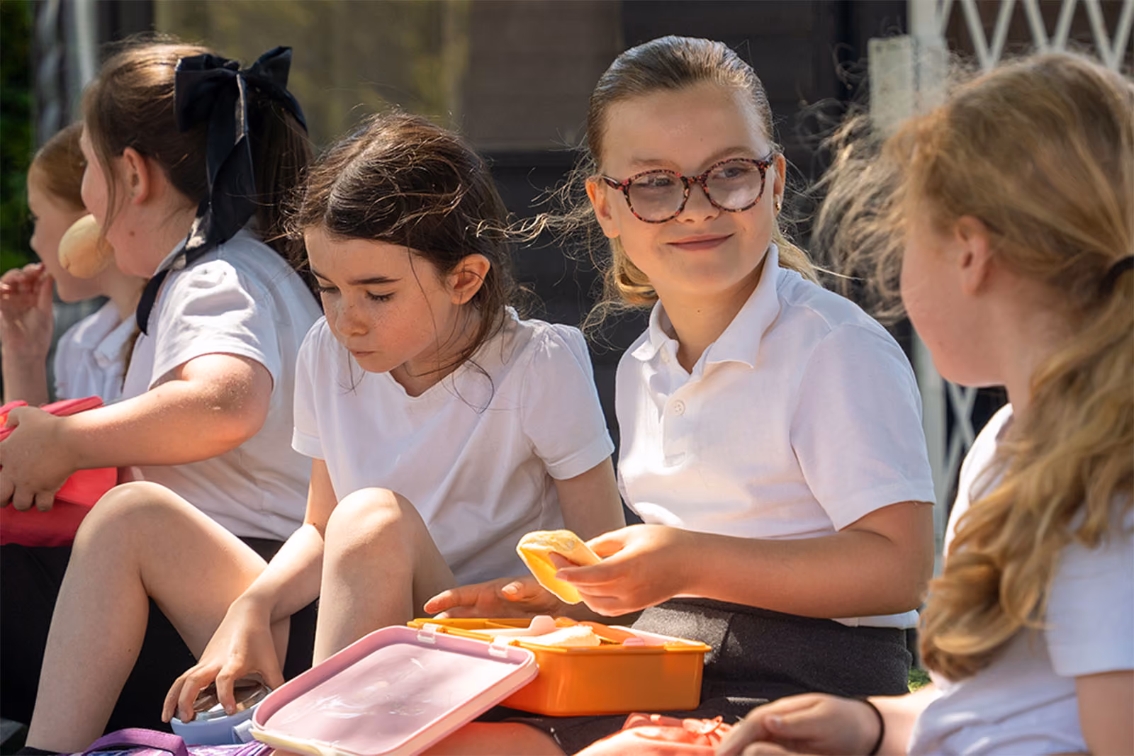 Pupils sitting outside eating packed lunches together.