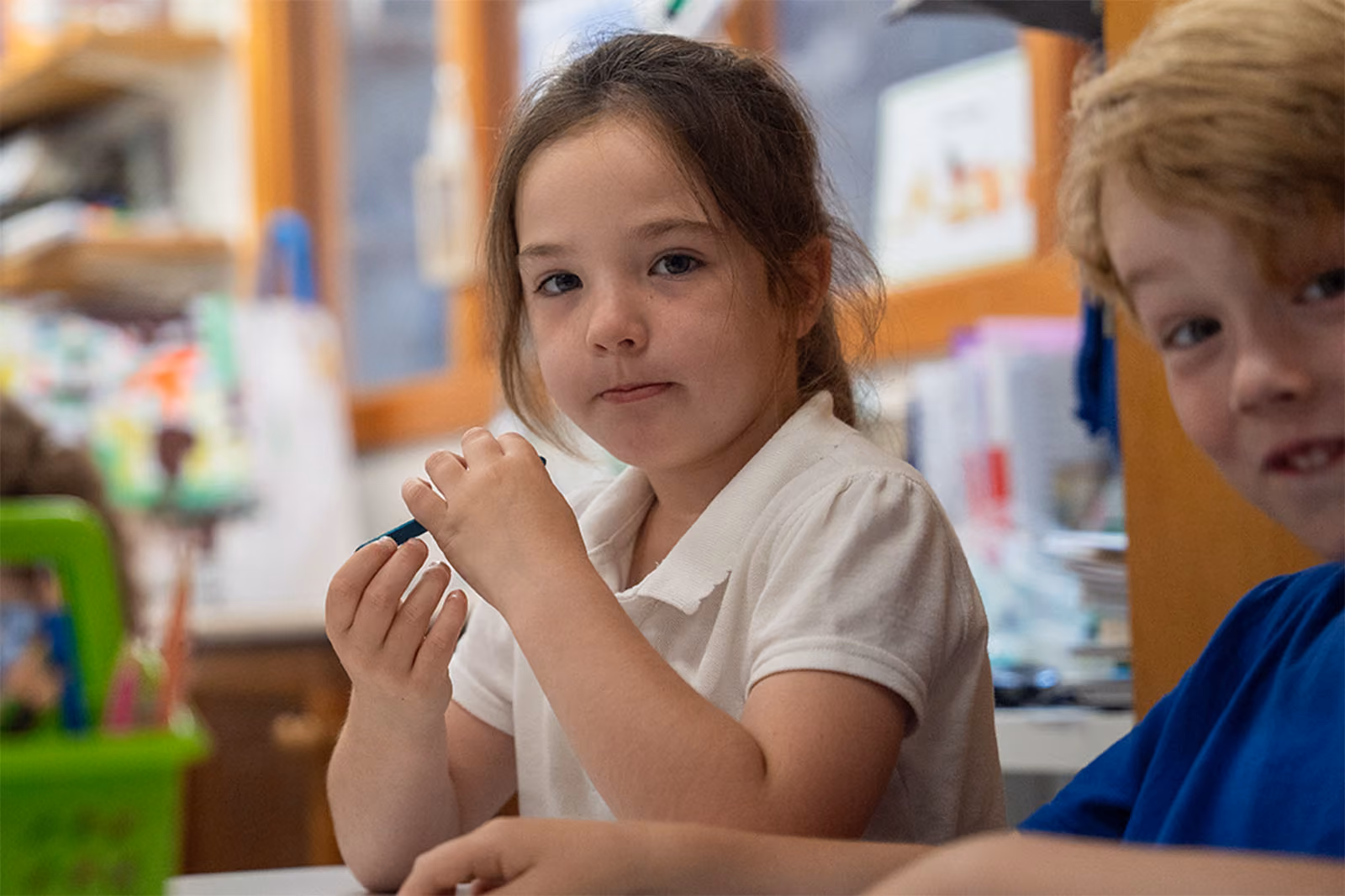 Pupil holding a pen looking at the camera, sitting beside another pupil in a classroom.