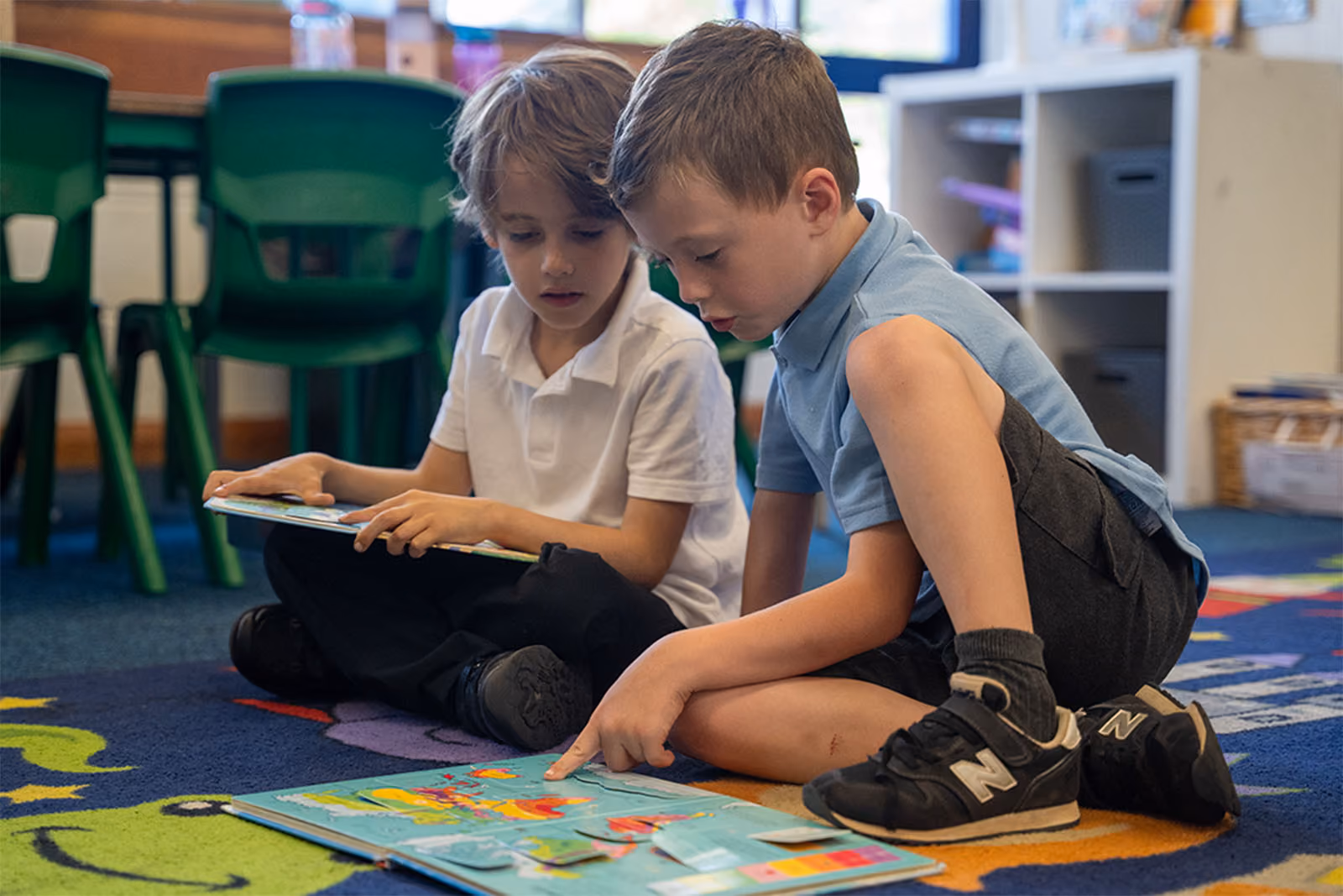 Two pupils sitting on the floor reading a book together.
