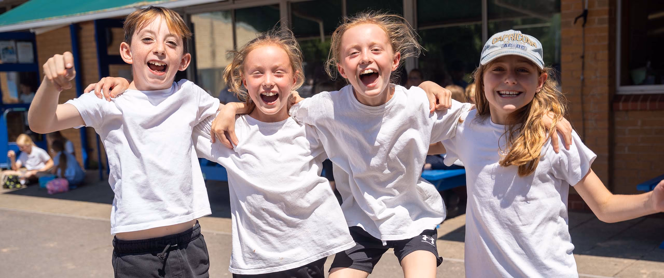 Four laughing pupils with their arms around each other in the school playground.