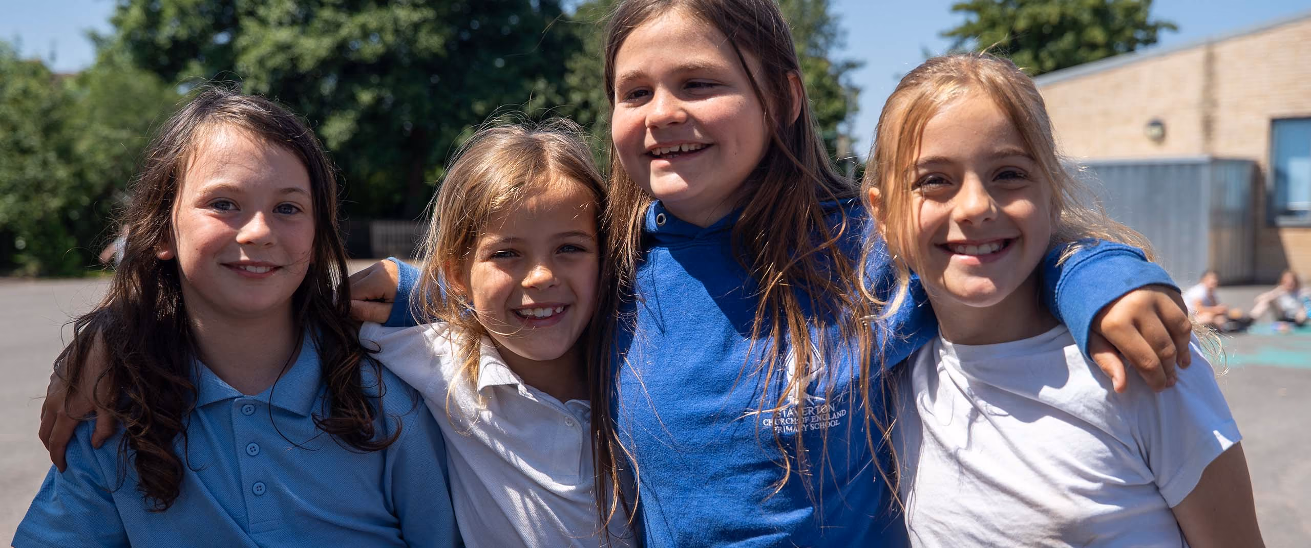 Four smiling pupils standing together with their arms around each other in the playground.