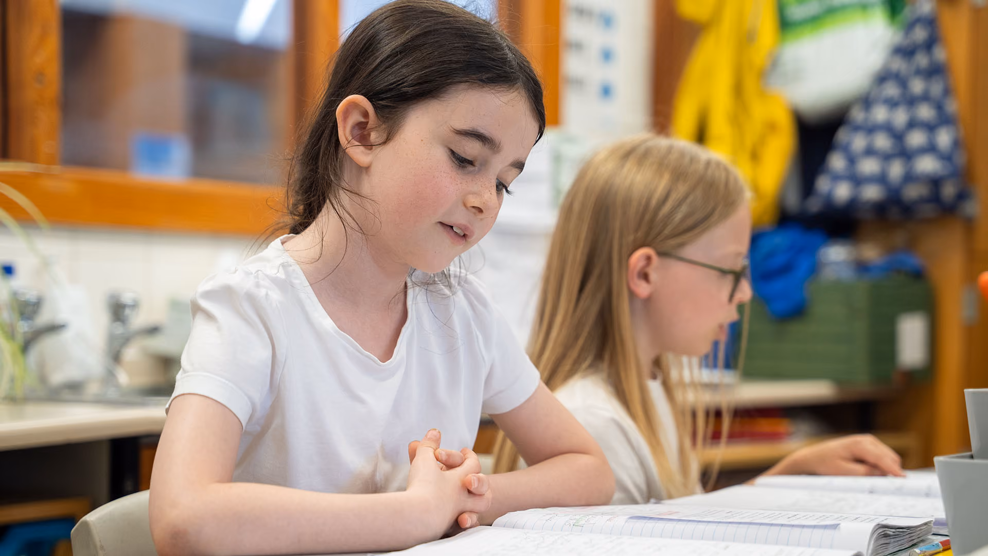 A girl and a boy sitting at a table reading and studying notebooks in a classroom setting.