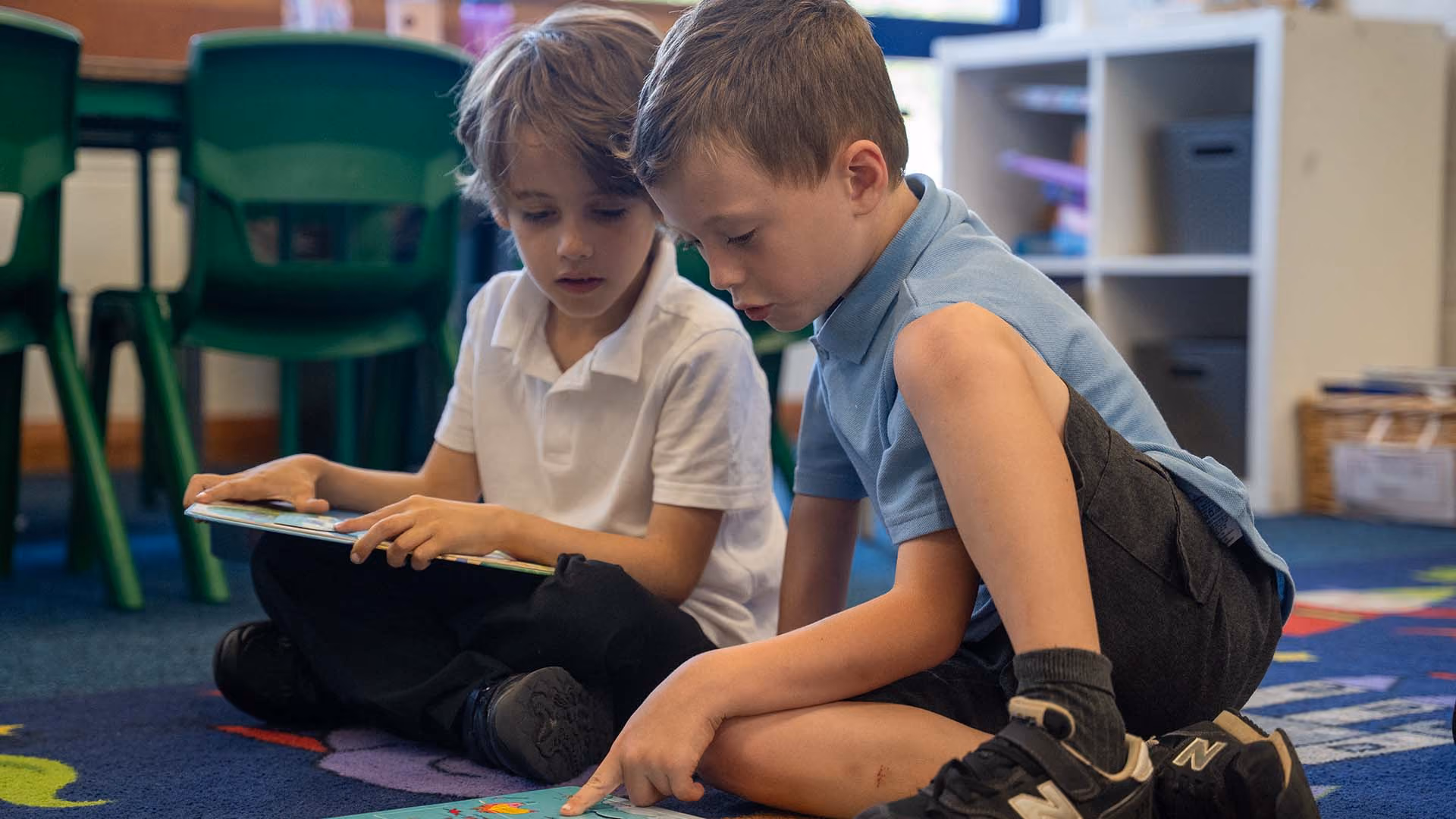 Two pupils sitting on the floor reading a book together.