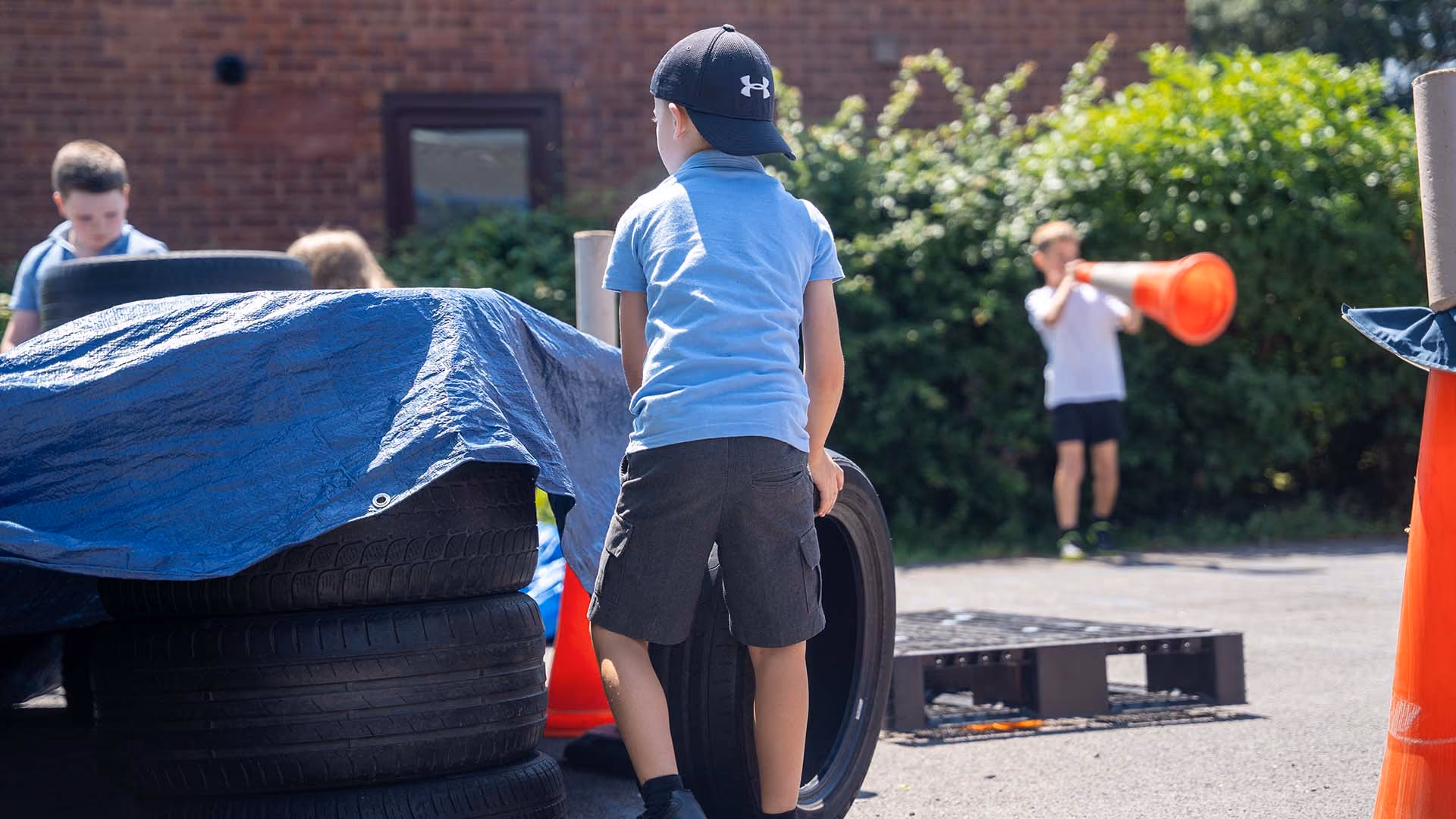 Pupils playing outdoors with tyres, a tarpaulin and traffic cones in the playground.