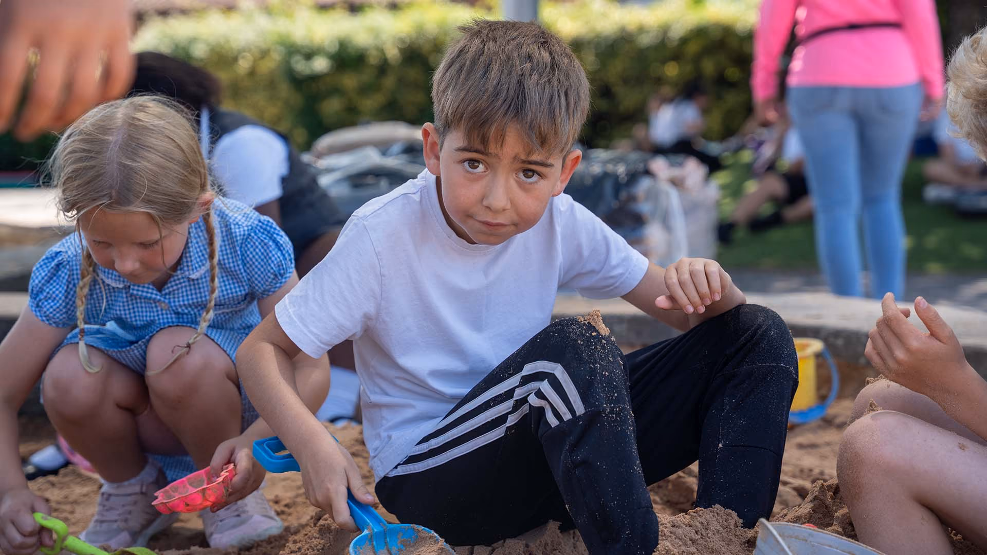 Pupils playing with sand and buckets in an outdoor sandpit.