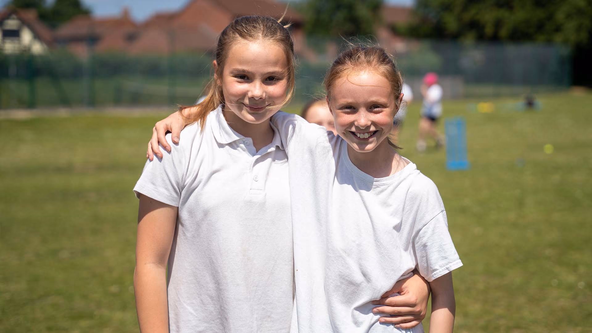 Two smiling pupils standing arm in arm on the playing field during a sports session.