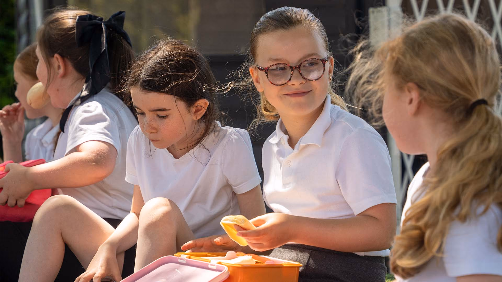Pupils sitting outside eating packed lunches together.