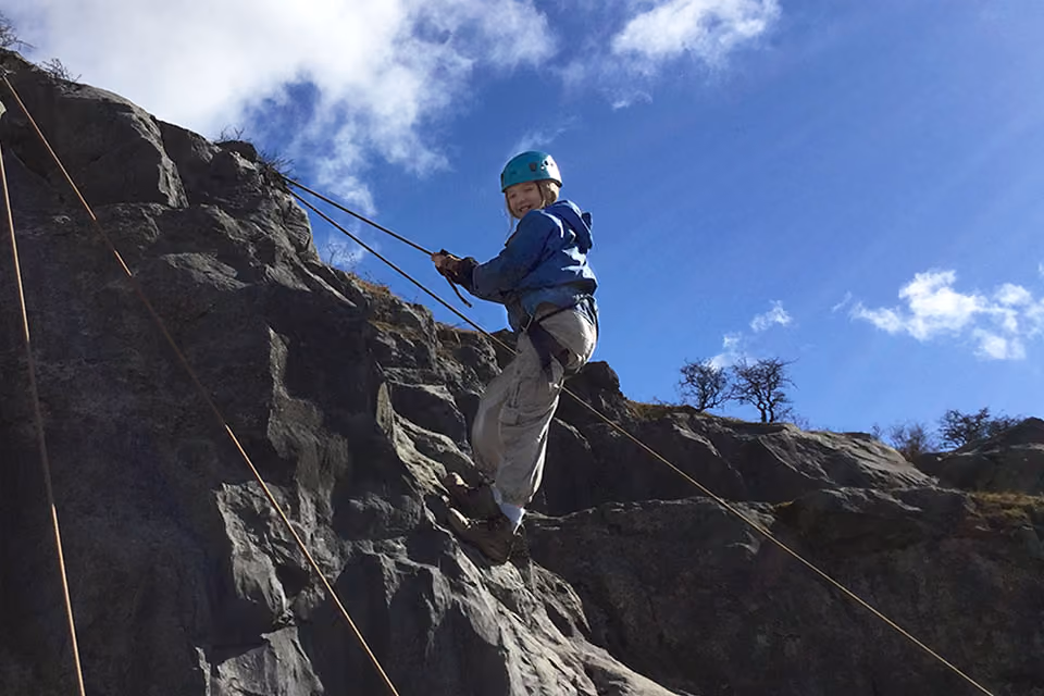 Pupil wearing a helmet and harness abseiling down a rock face on a residential trip.