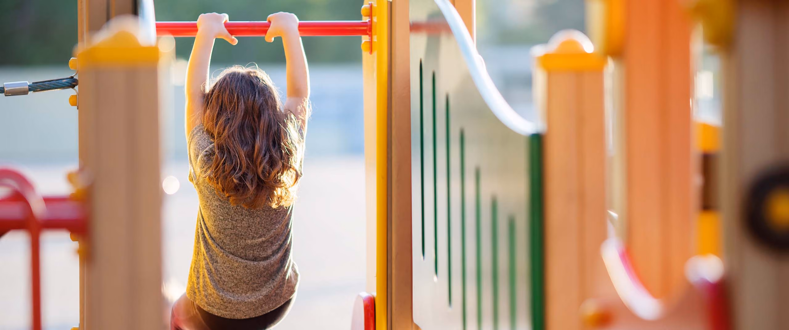 Child hanging from monkey bars on outdoor playground equipment.