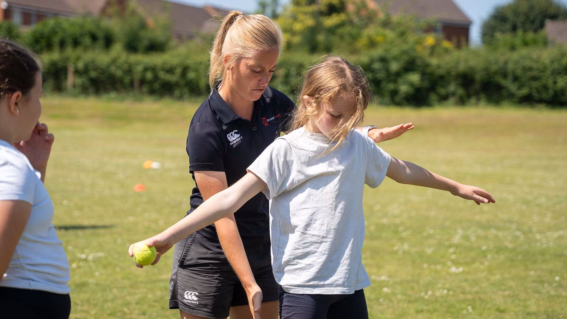 Coach demonstrating a throwing action to pupils during an outdoor PE lesson.