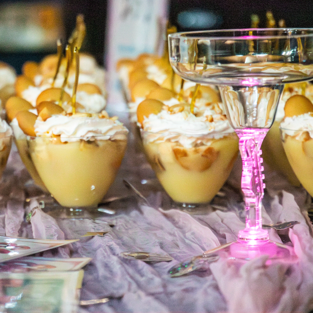 A close up of banana pudding, a specialty guitar cup, and the event menu placed on a table.