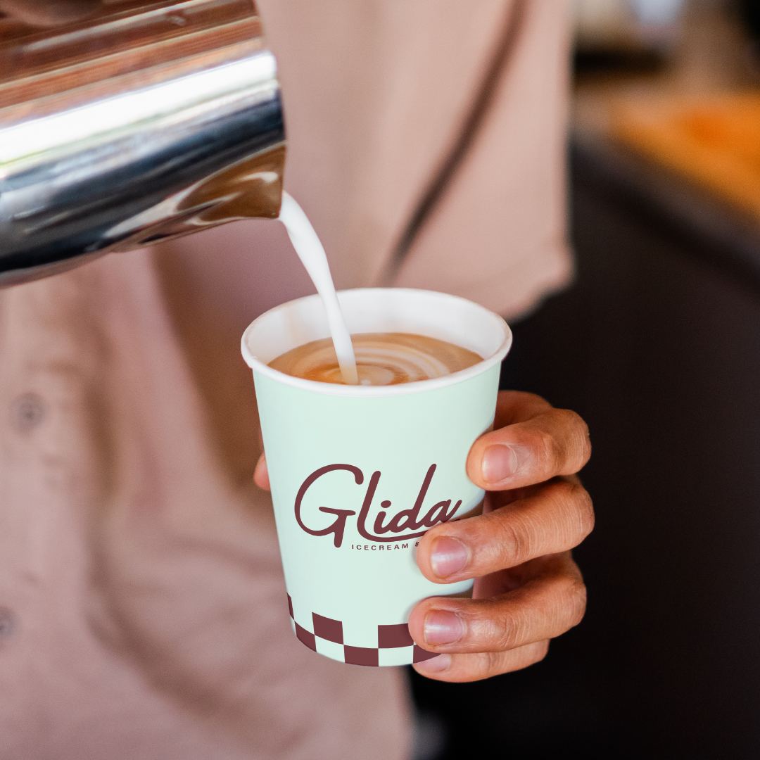 Mockup of a man pouring milk into a disposable coffee cup with the Glida's logo on it.
