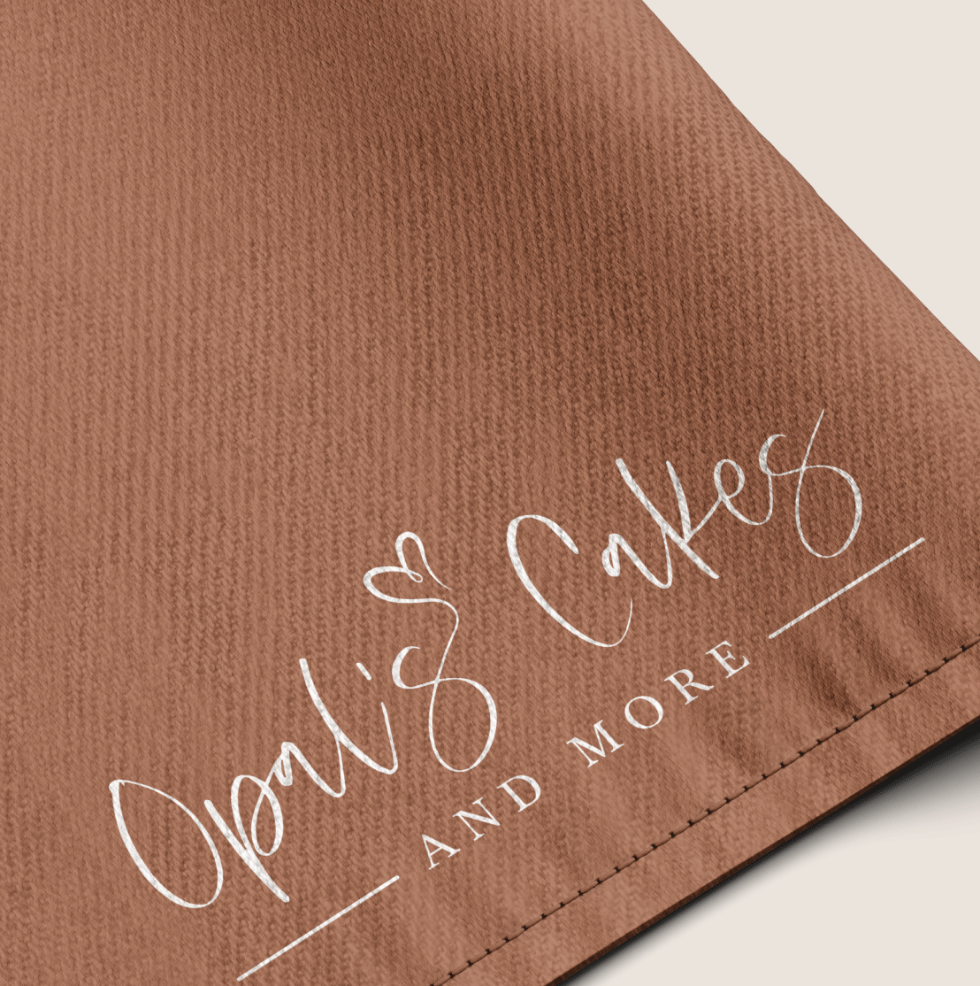 Mockup of a brown apron with the Opal's Cakes and More logo.