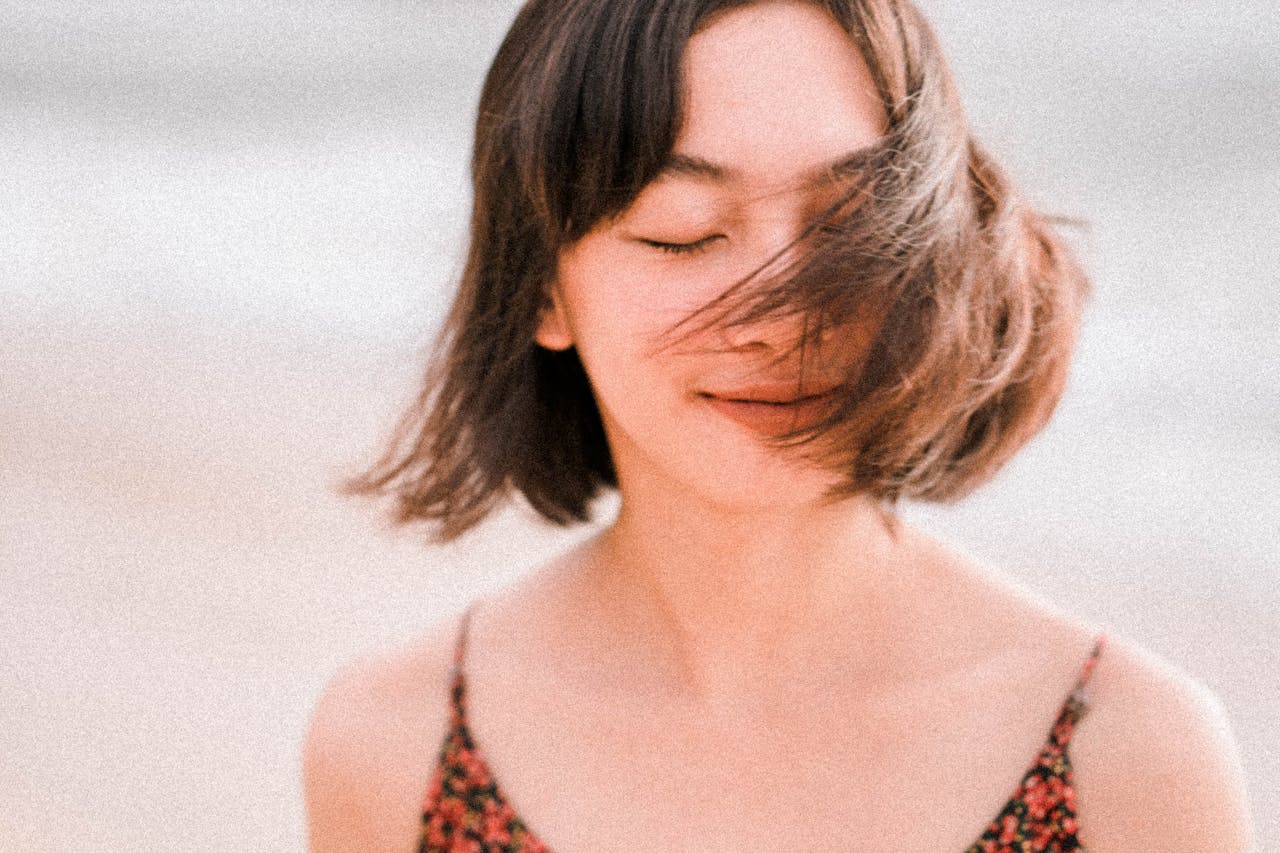 A woman standing on a beach with her eyes closed.