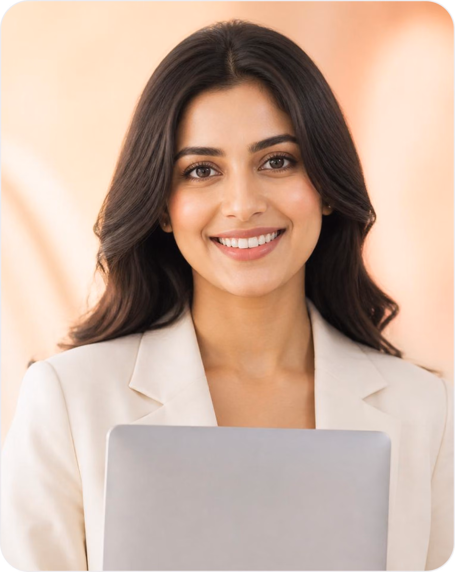 Smiling woman with dark hair wearing a beige blazer, holding a silver laptop.
