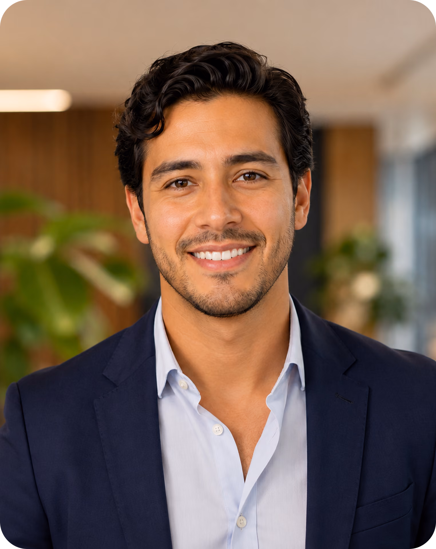 Smiling man with dark hair in a blazer and light shirt in an office setting.