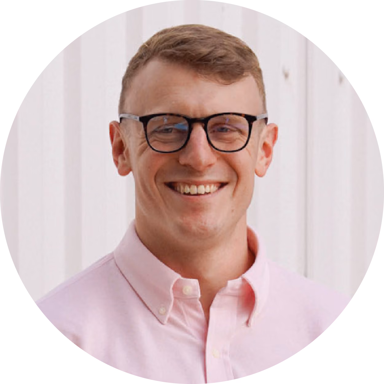 Smiling man wearing glasses and a light pink button-up shirt against a light background.