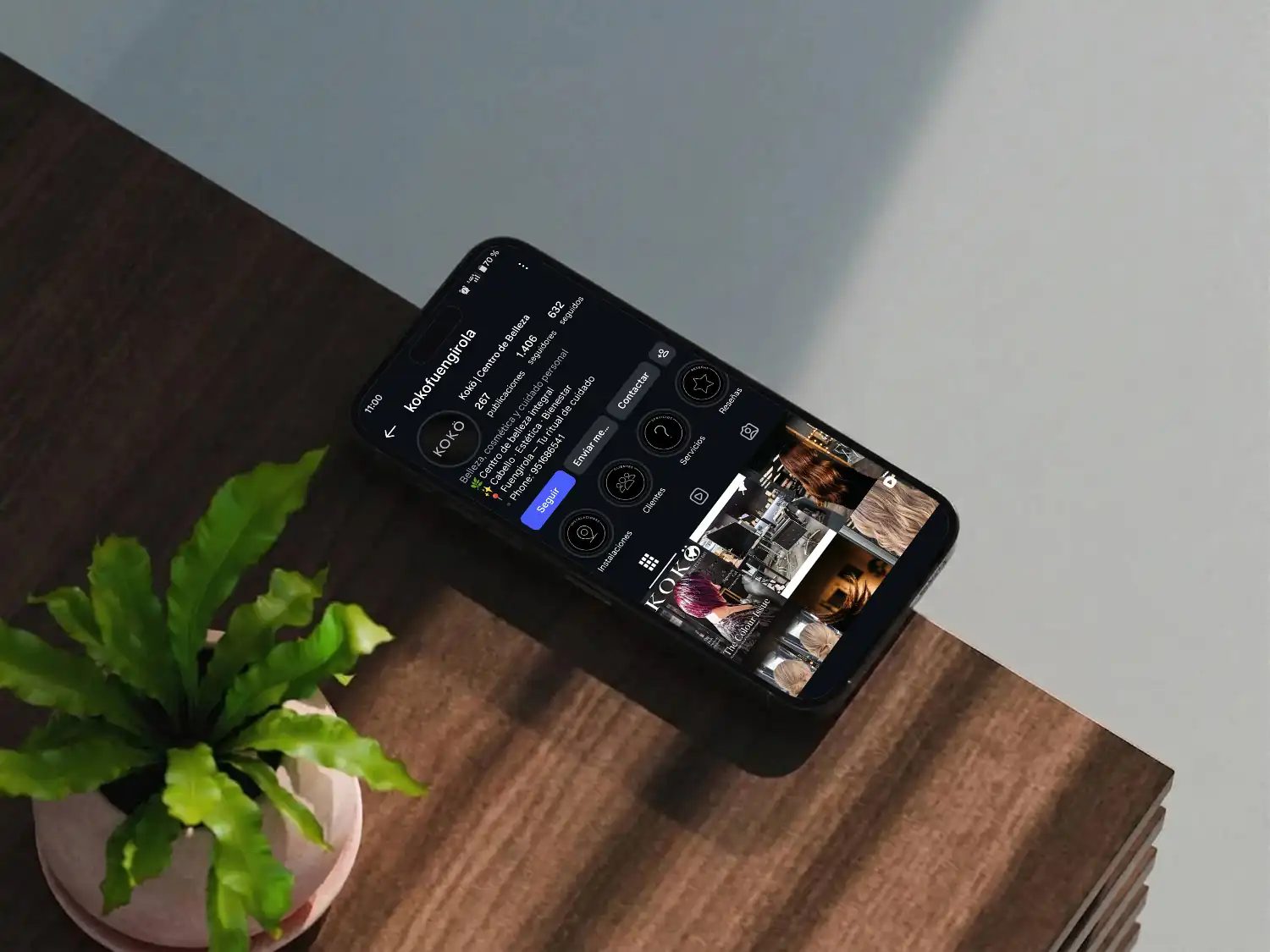 iPhone apoyado junto a una planta sobre una mesa de madera mostrando un feed de Instagram