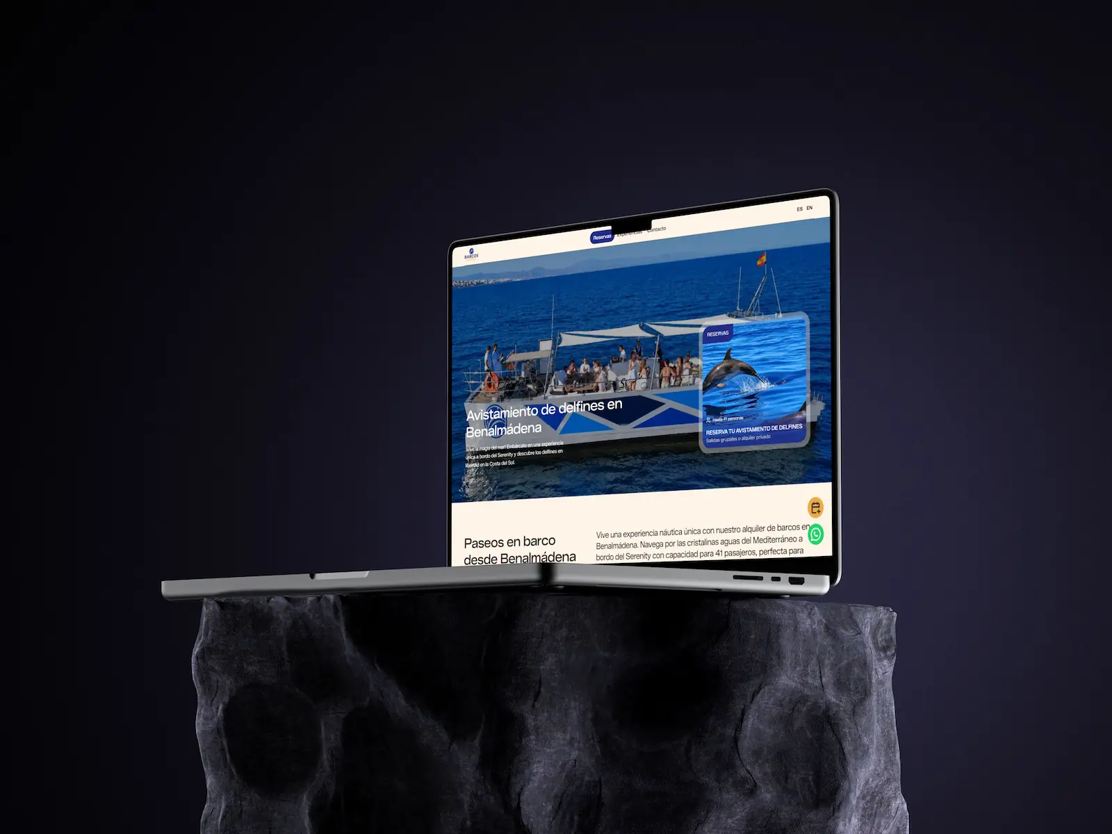MacBook Pro sobre un pedestal de roca mostrando la web de Barcos Málaga