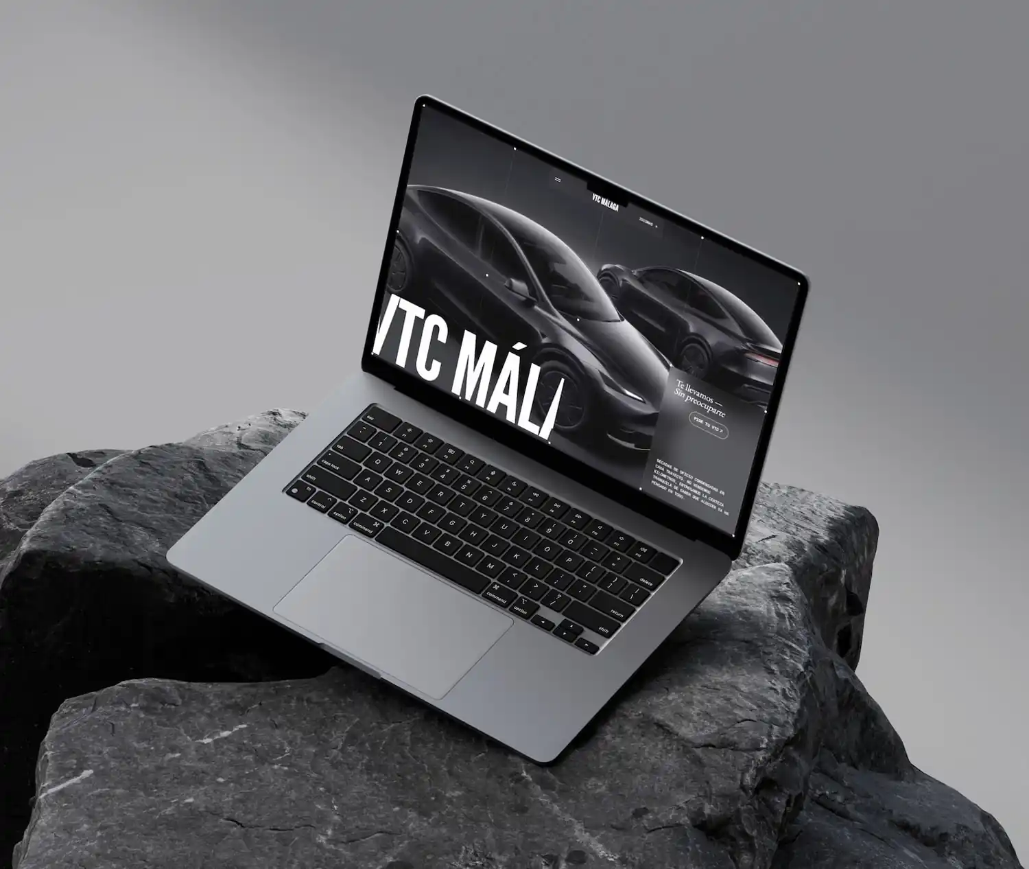 MacBook apoyado sobre rocas mostrando la web de VTC Málaga