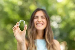 Woman holding a clear aligner toward the camera